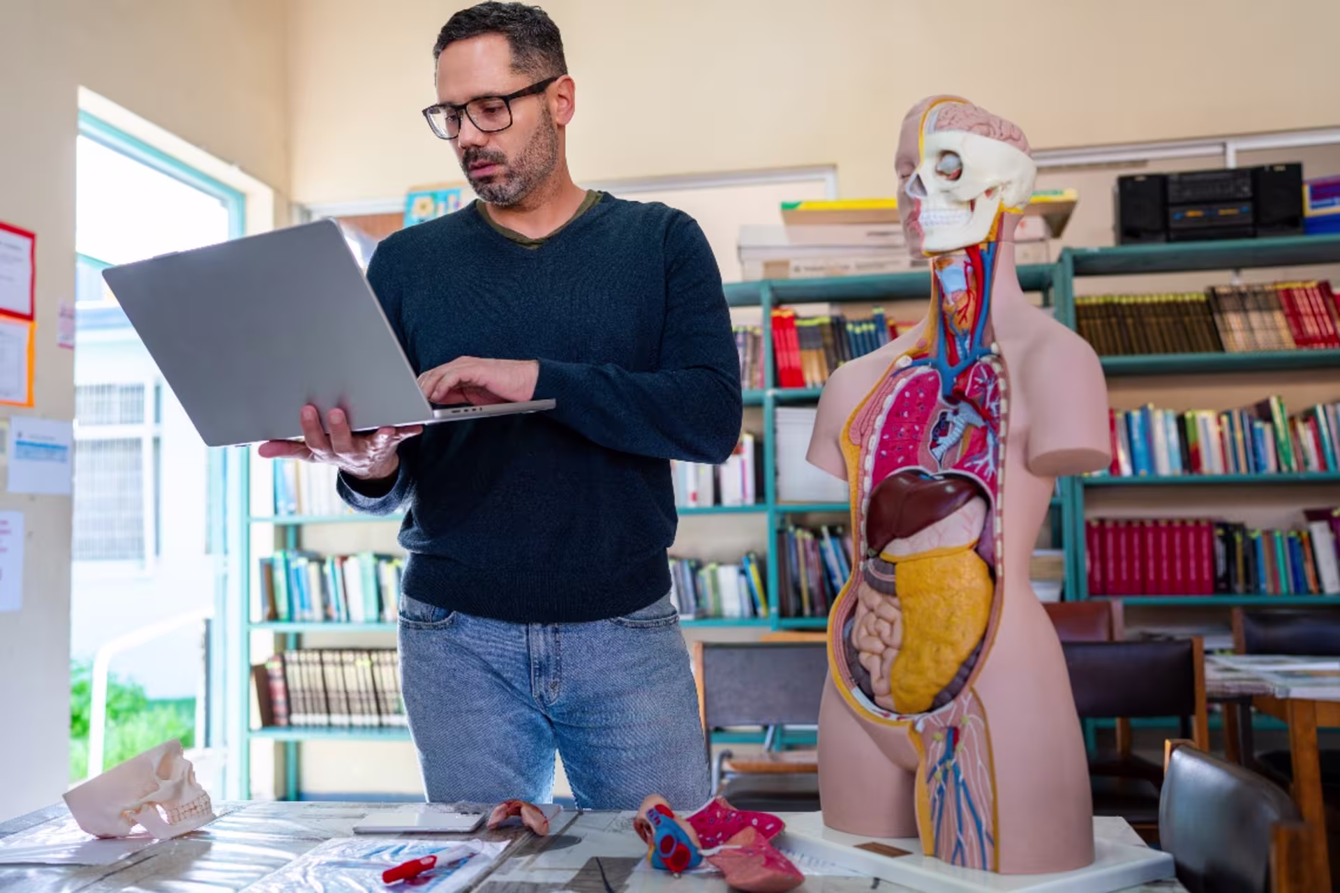 Male pre-nursing student holding a laptop at home while working on anatomy coursework. 