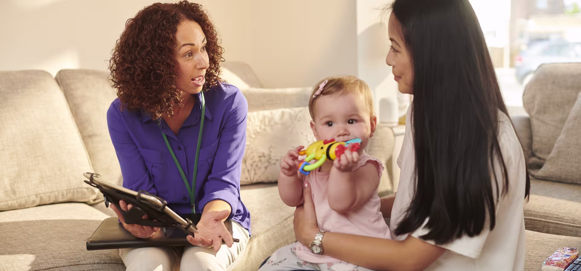 A woman cradles a baby while another woman looks at a tablet, suggesting a nurturing and educational environment.