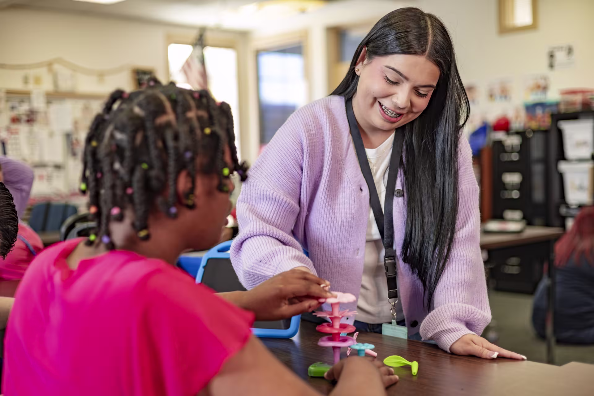 Female social worker assisting a child with hands-on learning activities at a classroom table.