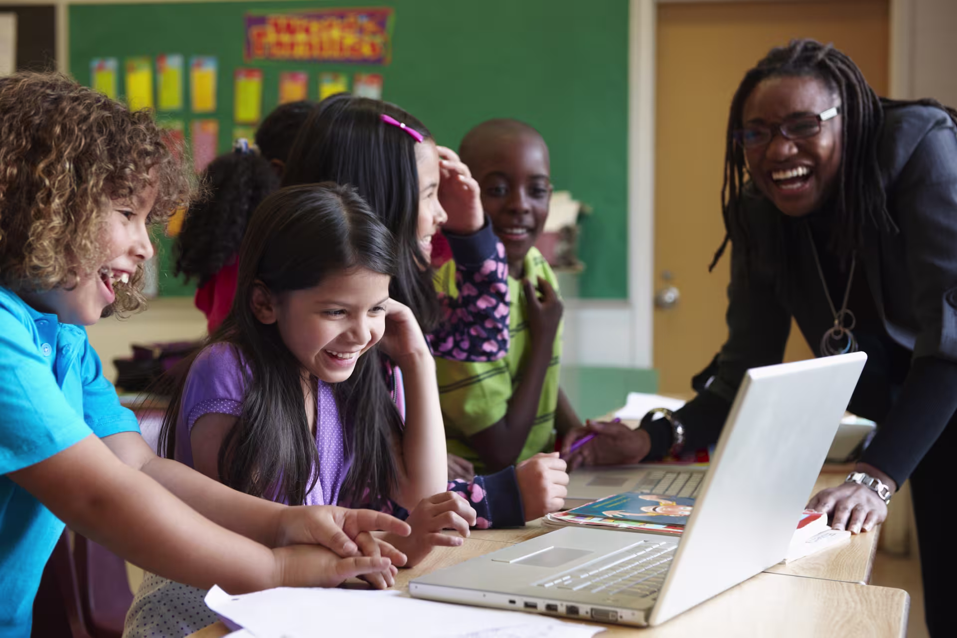 A teacher guides students as they work together on a laptop activity.