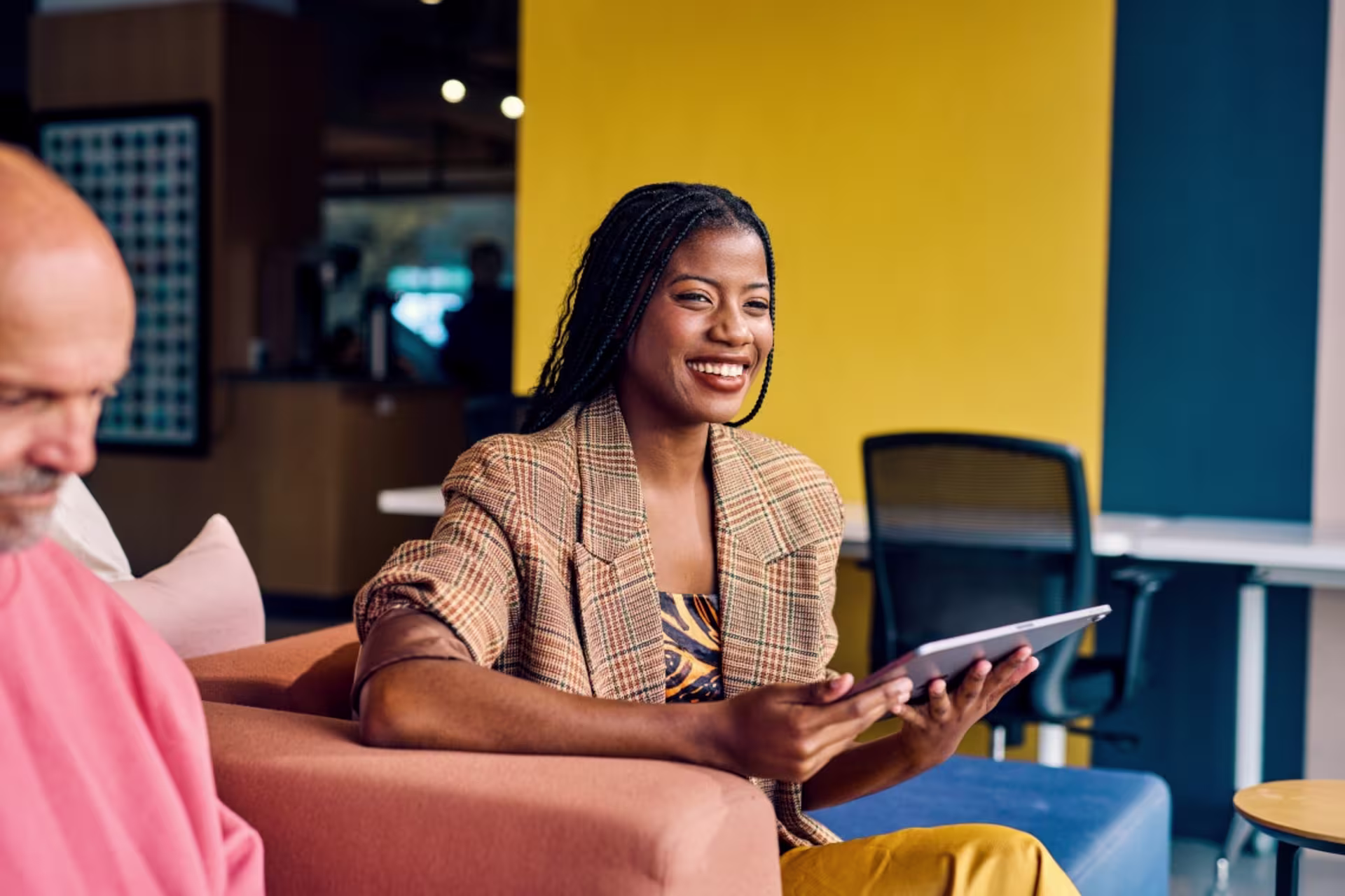 A female entrepreneur smiles while holding a tablet during a collaborative discussion in a modern office lounge.