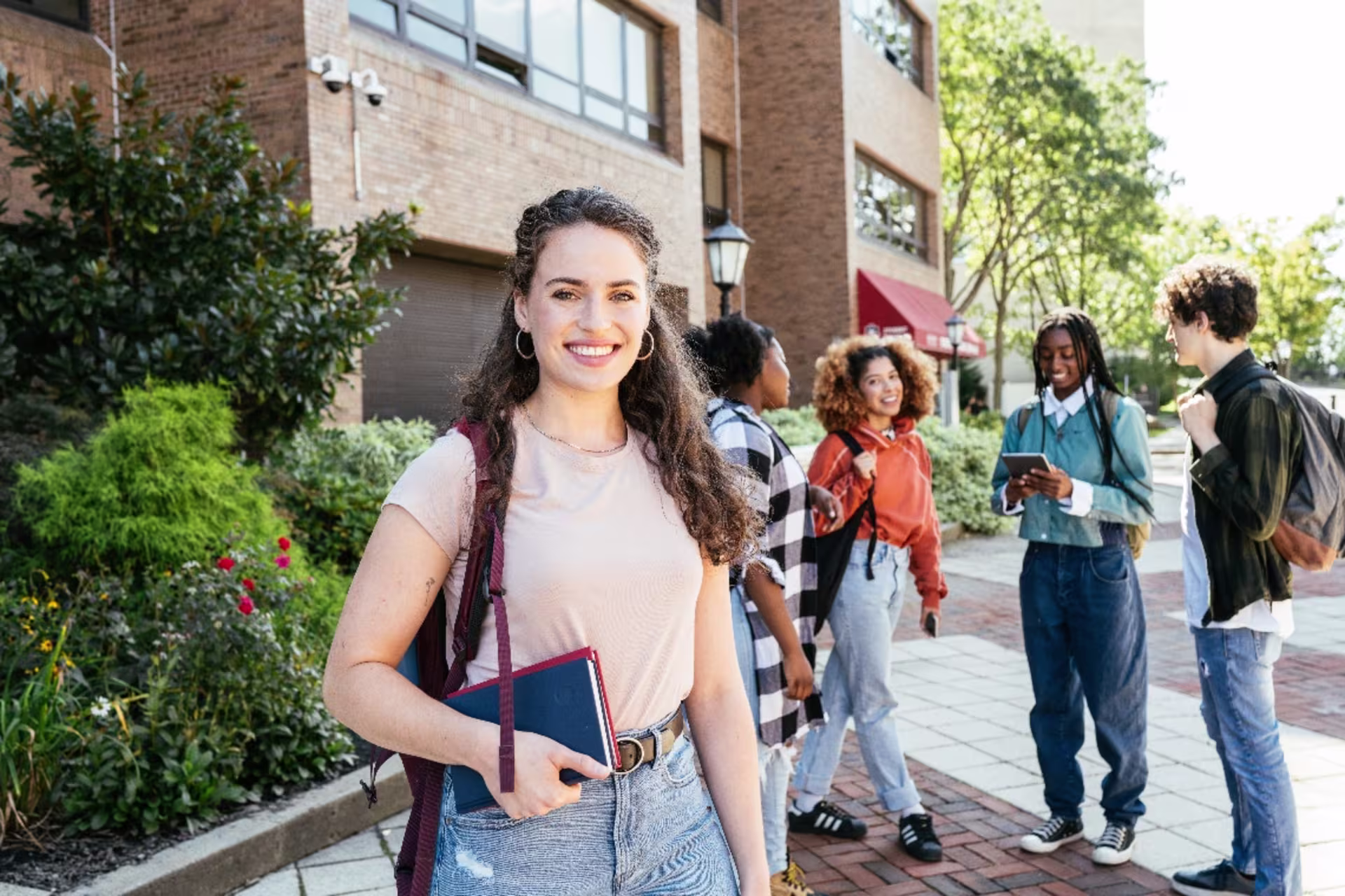 A risk management student holds textbooks on campus with classmates in the background.