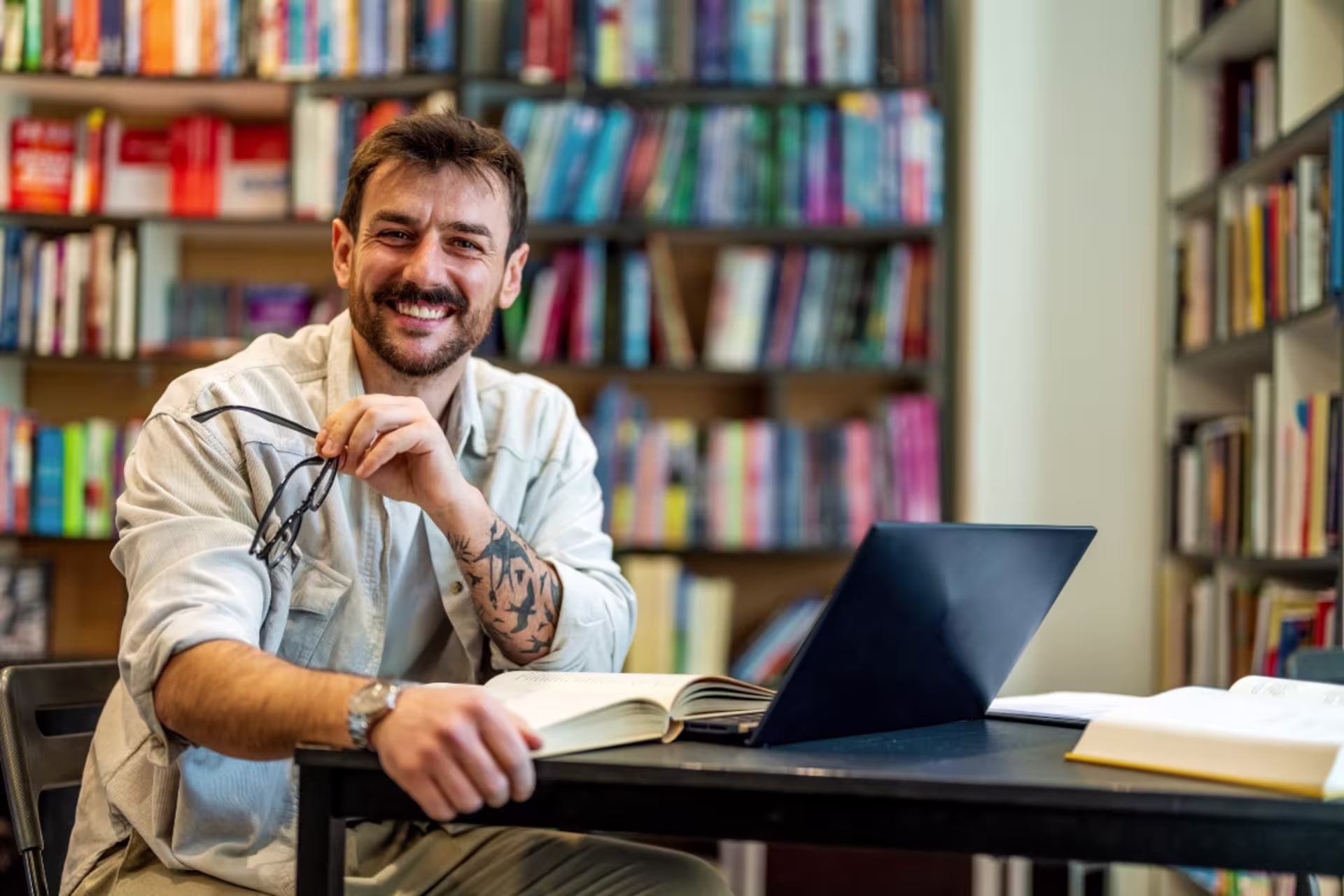 History education student sitting at a desk with books in front of a large bookshelf filled with historical and academic texts.