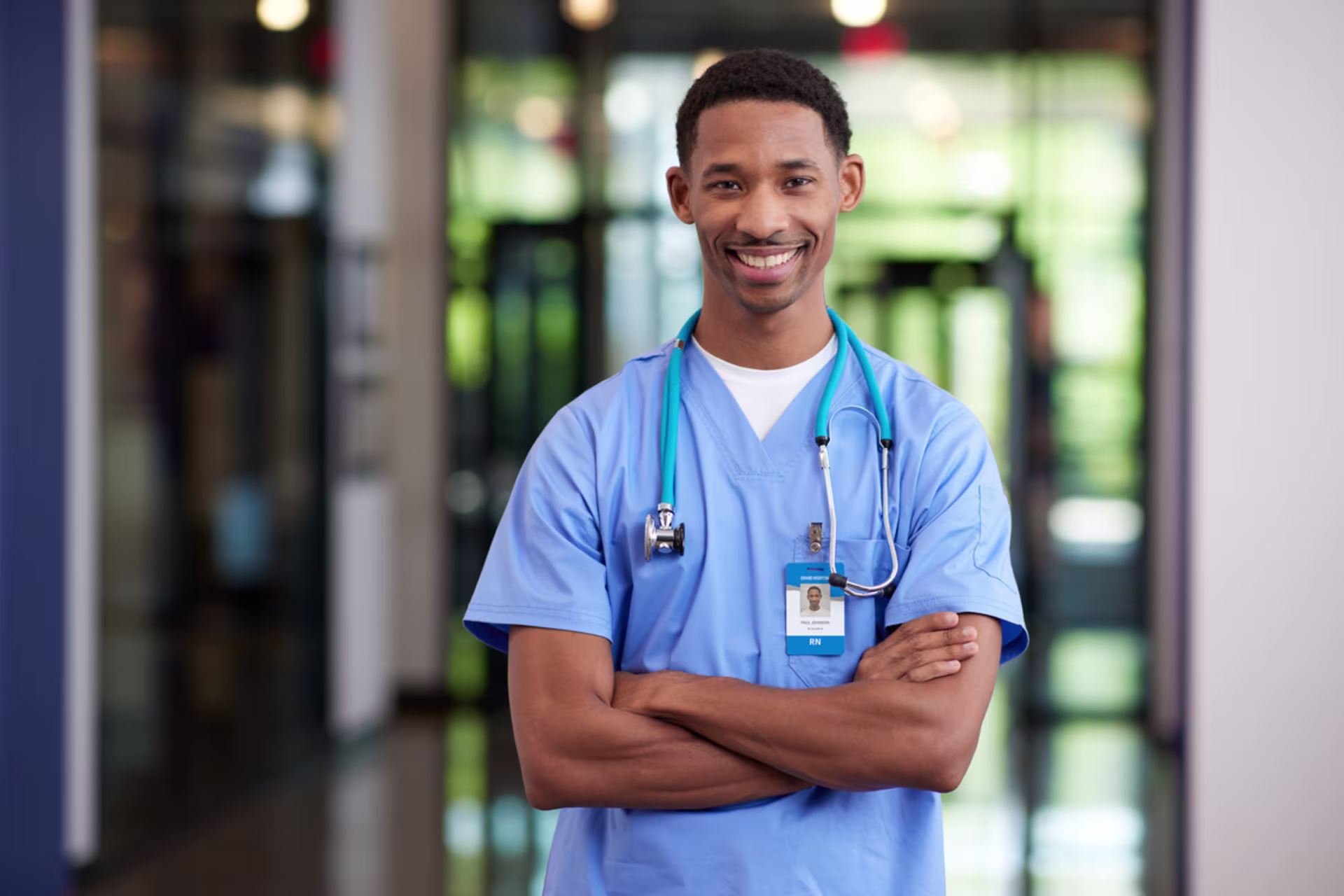 A nurse in blue scrubs with a stethoscope stands in a medical clinic.