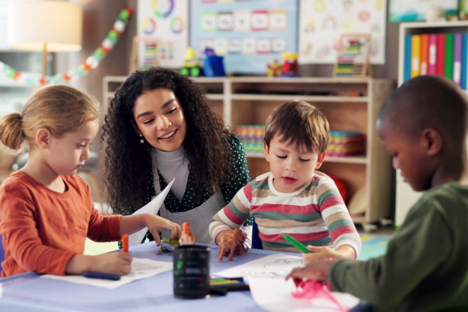 A teacher guides young children as they draw and work on art activities in an early childhood classroom.