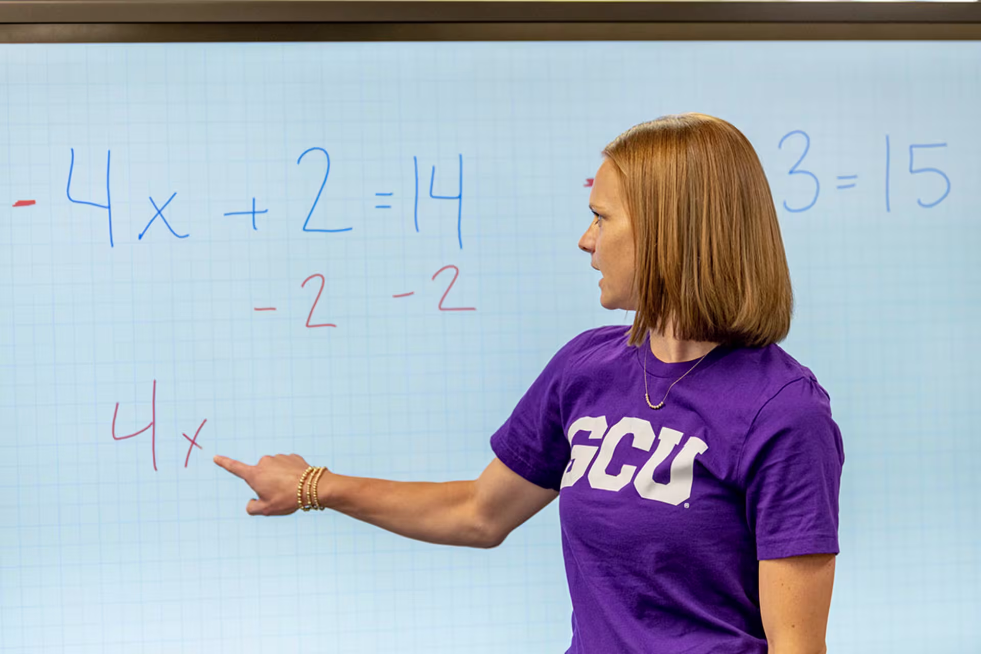 Female GCU math teacher explaining problem to her class on a whiteboard.