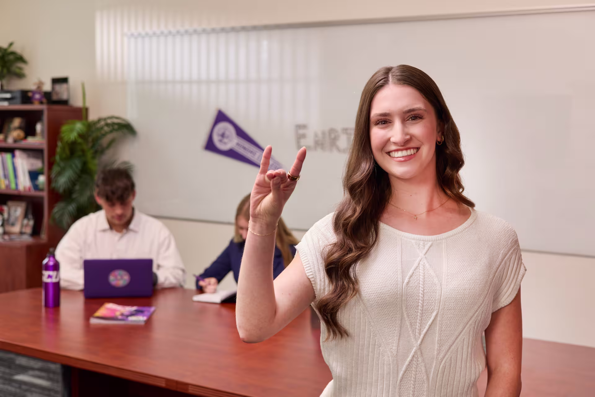 Female graduate higher education leadership certificate student smiling with classmates working in the background.