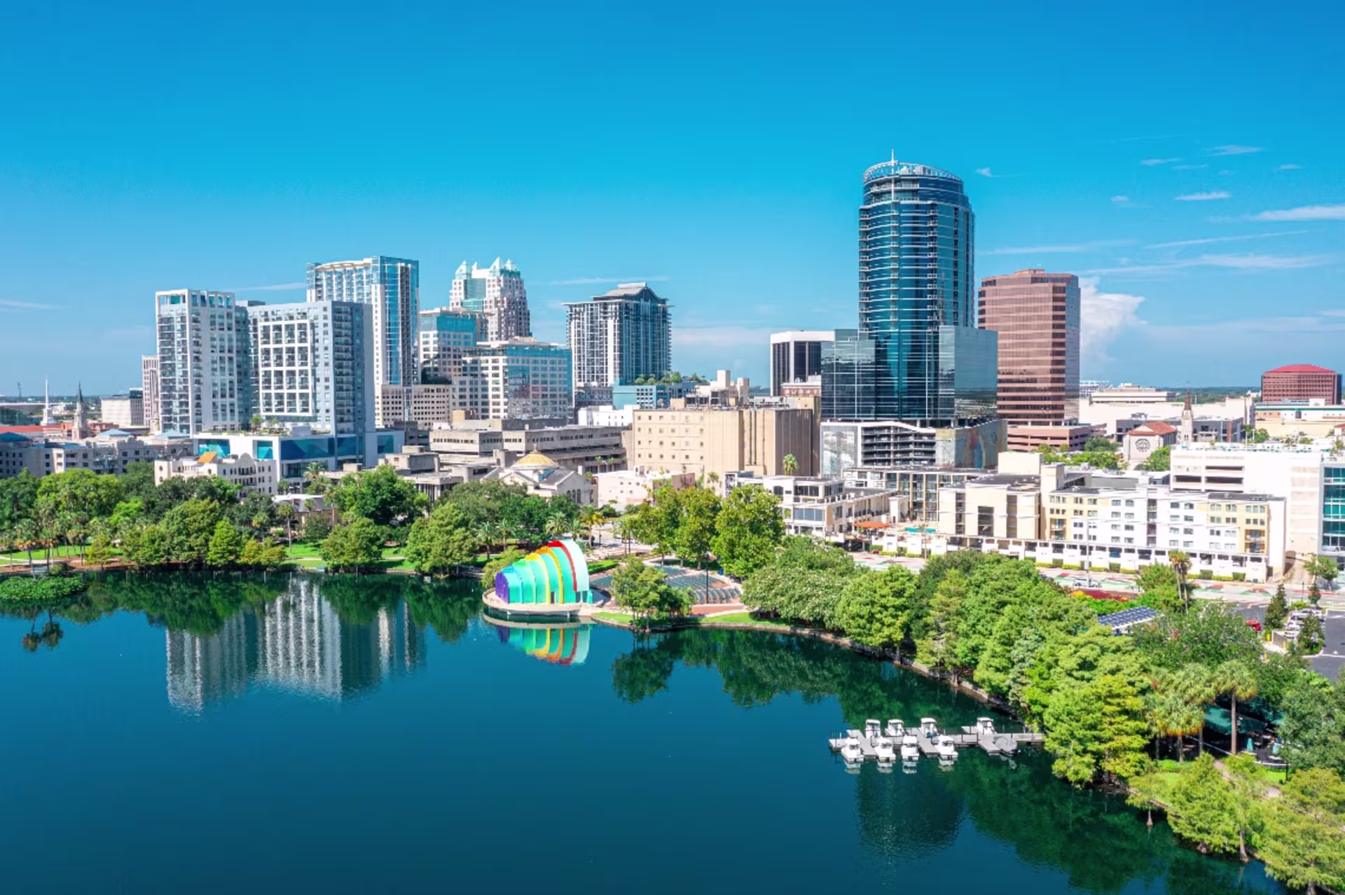 An aerial view depicts the downtown Orlando skyline with Lake Eola, a fountain and surrounding city buildings on a clear day.