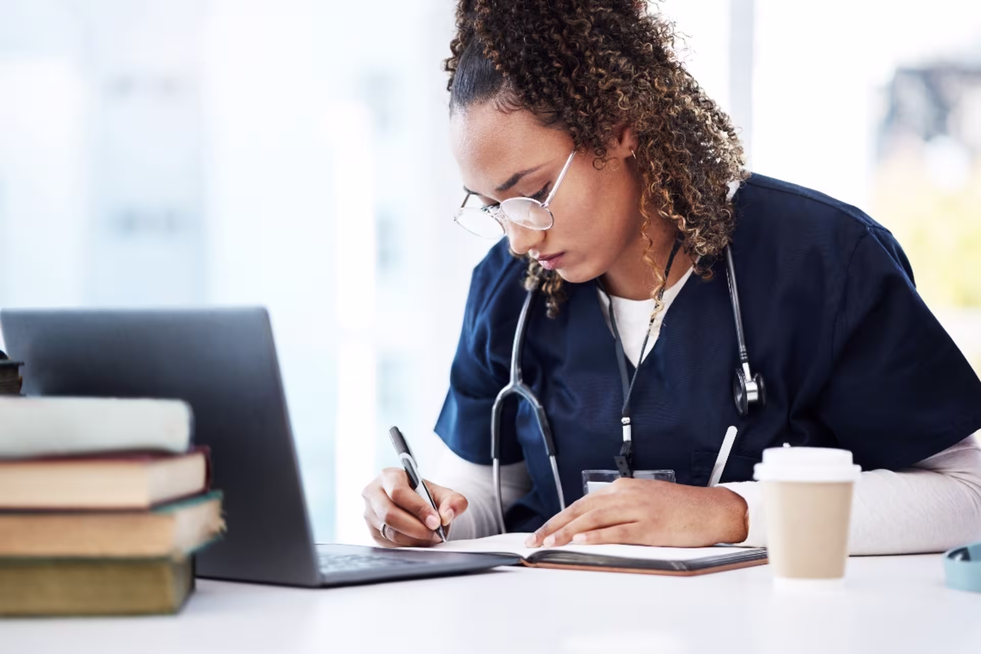 A GCU health informatics student wearing navy scrubs studies with a laptop and notes.