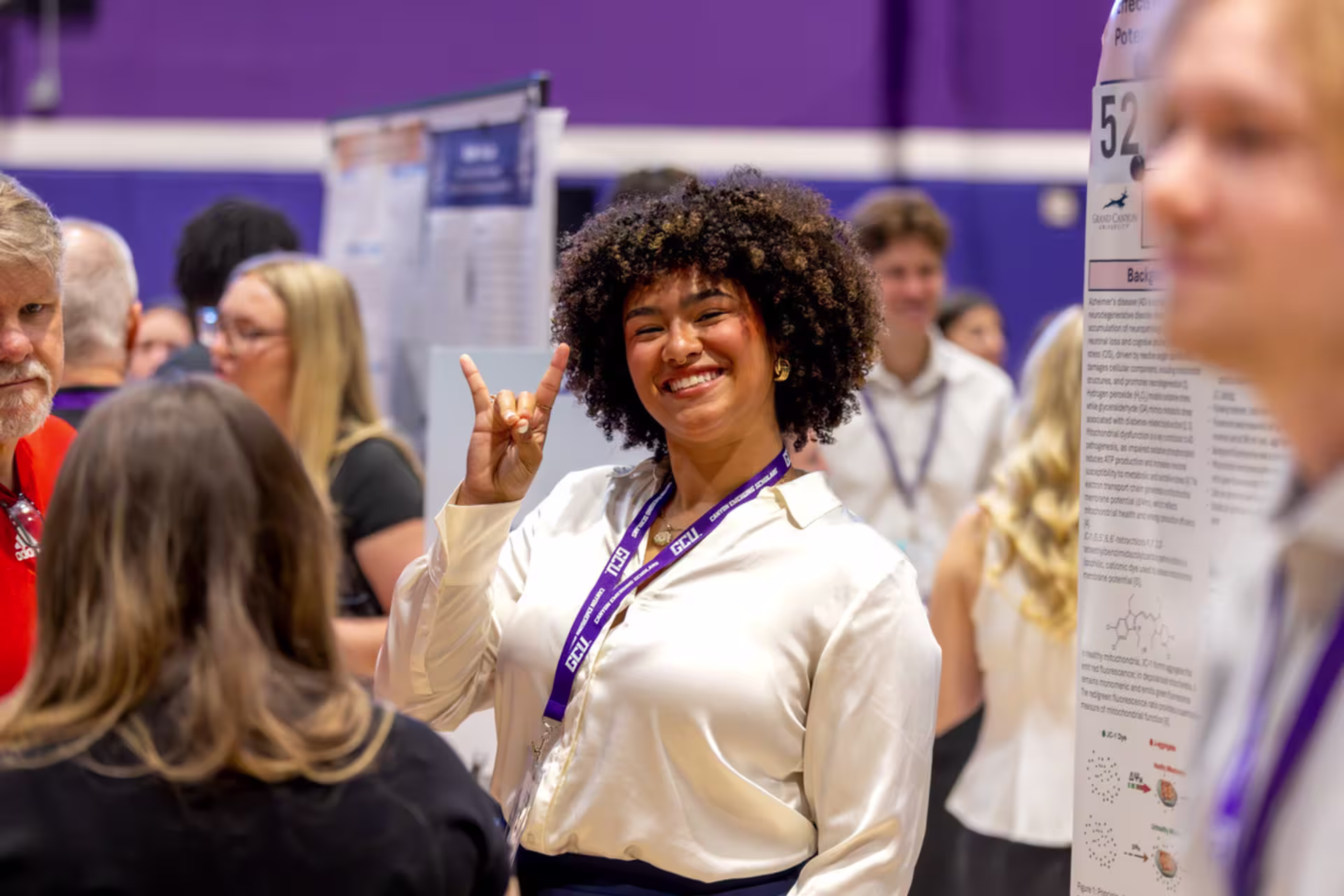 A female GCU business student at a business event holds the Lopes Up sign and smiles at the camera.