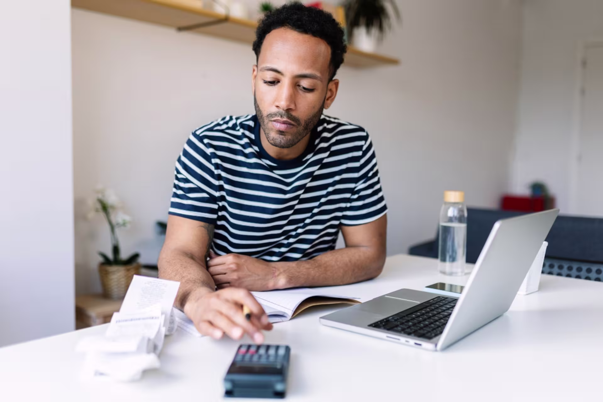 A pre-PA student calculates expenses at a desk with a calculator, receipts and a laptop, managing personal finances at home.