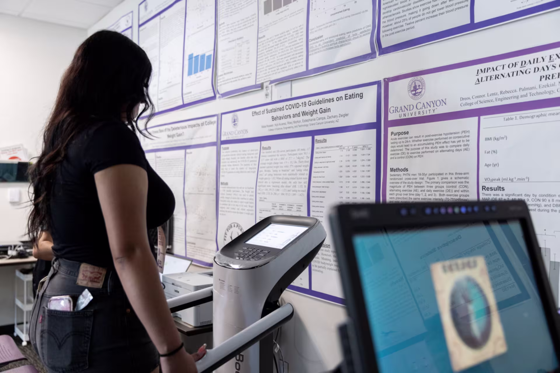 A female exercise science student in a GCU classroom learns while using a fitness machine.