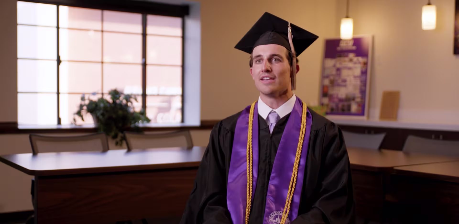 Bradley Robertson sitting in a room in his graduation cap, gown and stoll.