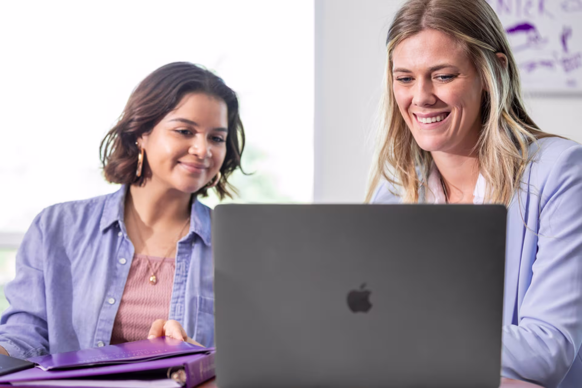 Two female business students sit next to each other and work on online coursework on a laptop.