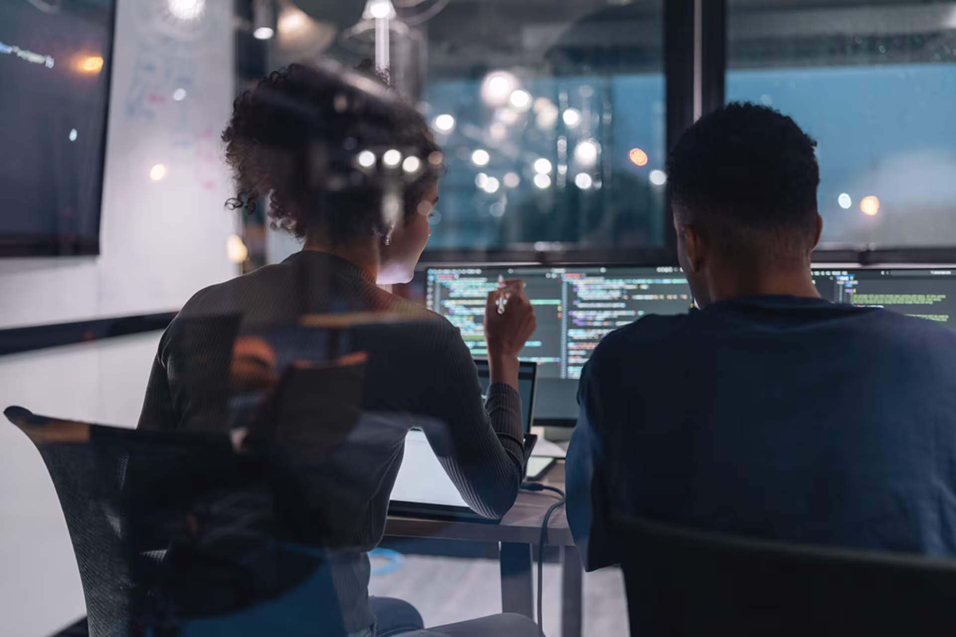 Infrastructure professional students collaborating on a laptop in a modern office with city skyline views, discussing work and digital strategy.