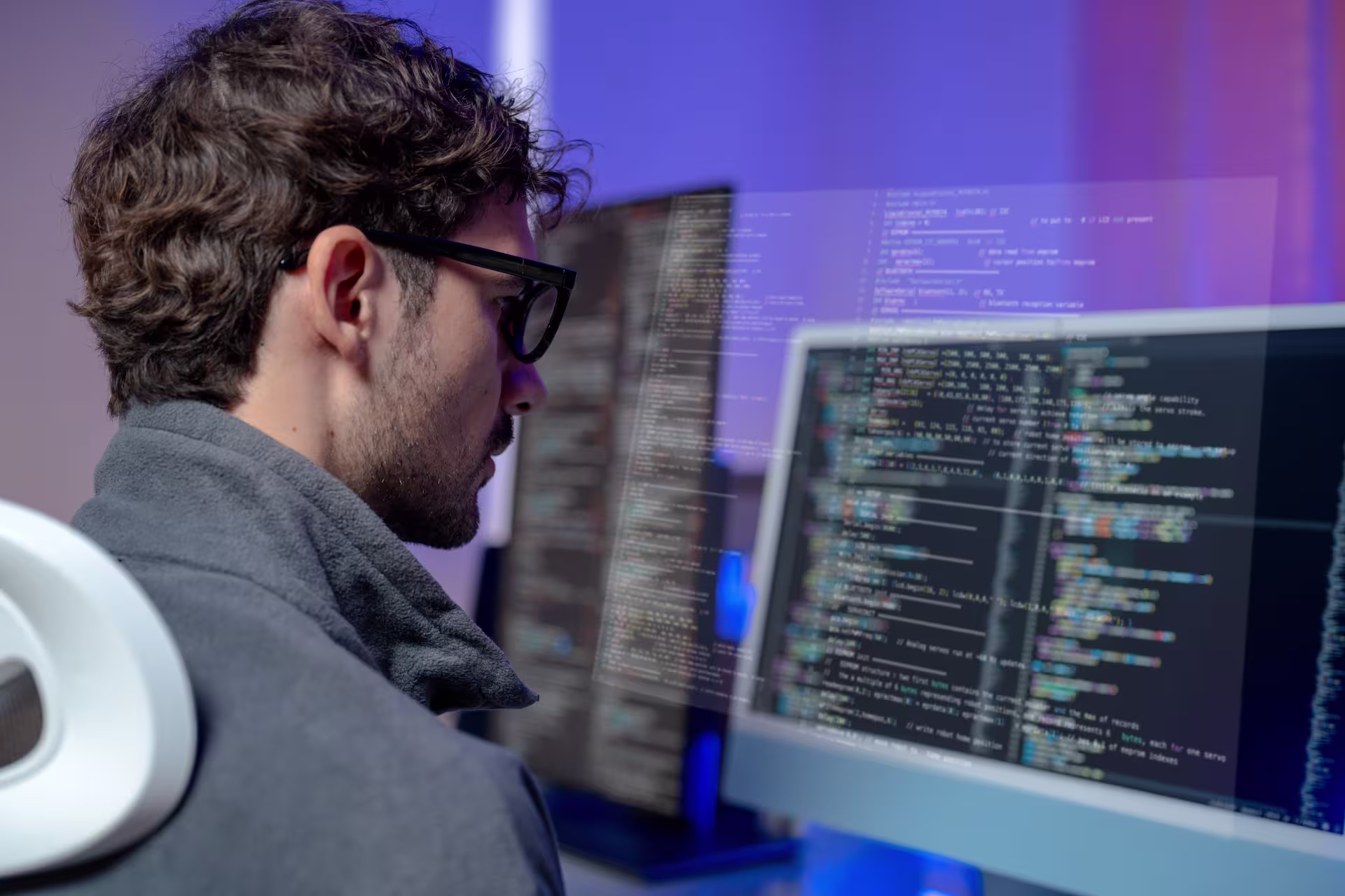 Infrastructure professional student working at a computer, reviewing and writing code on multiple monitors in a modern workspace.