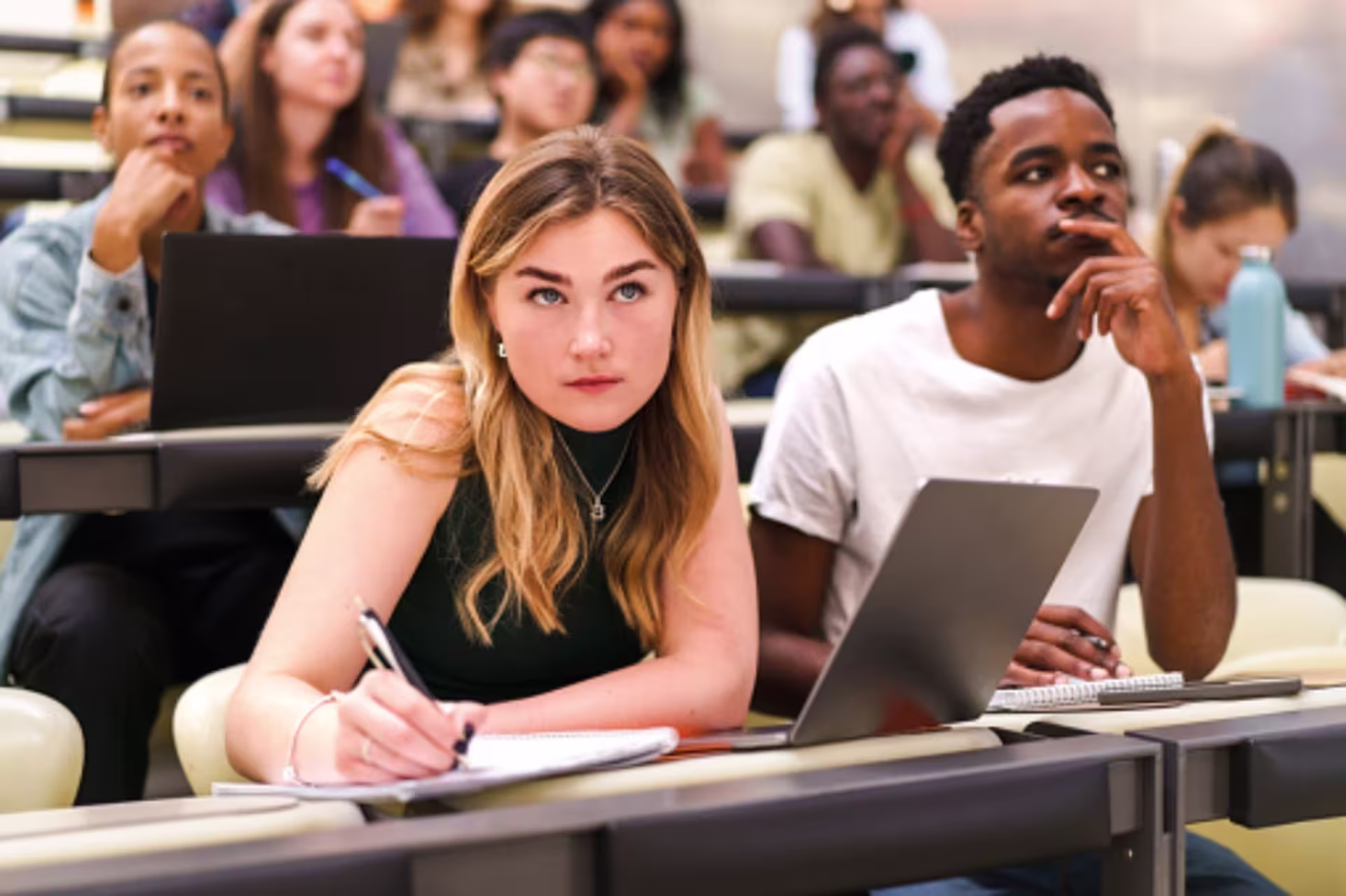 Students taking notes on laptops during a college lecture.