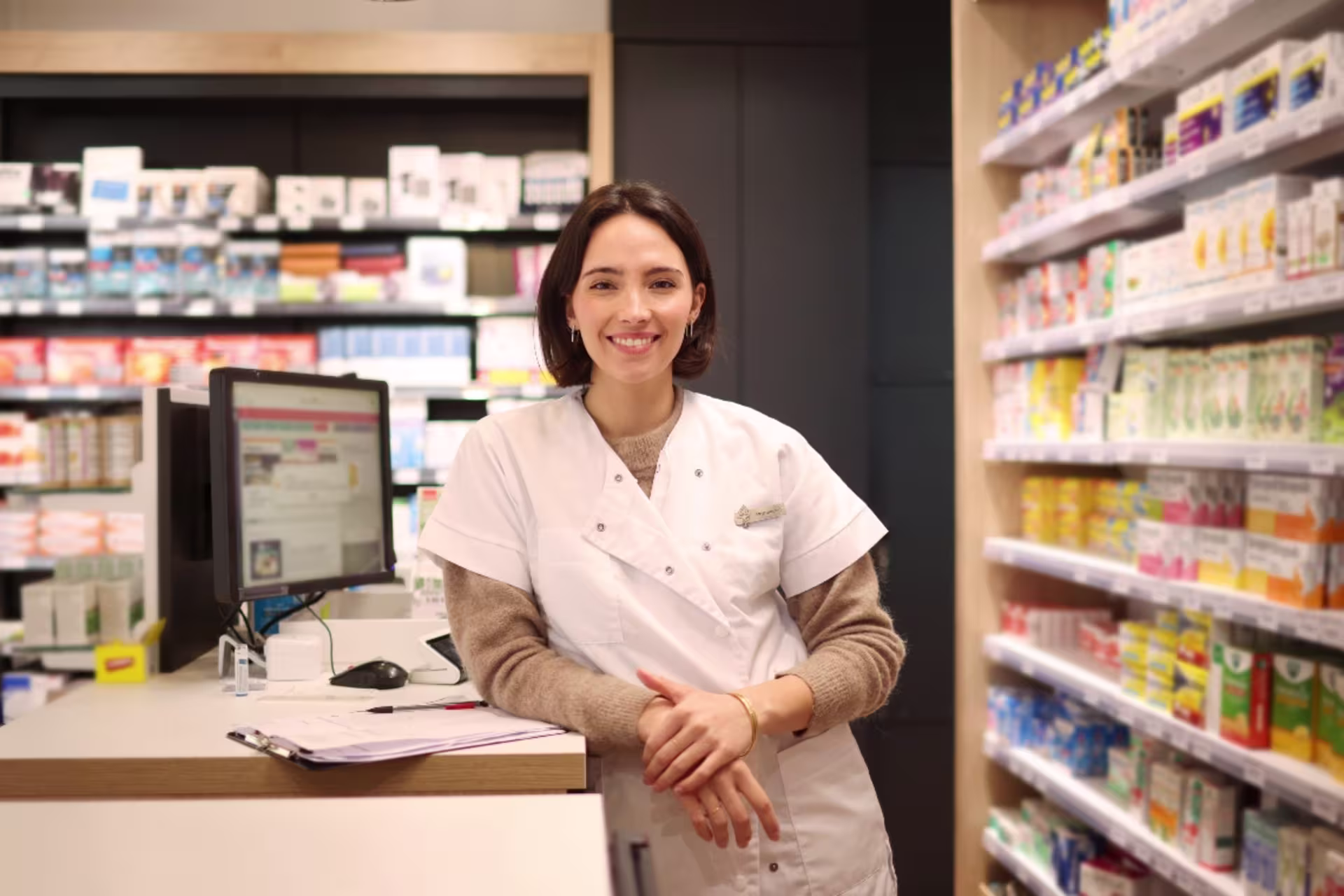 A female healthcare professional assists patients at a pharmacy counter.