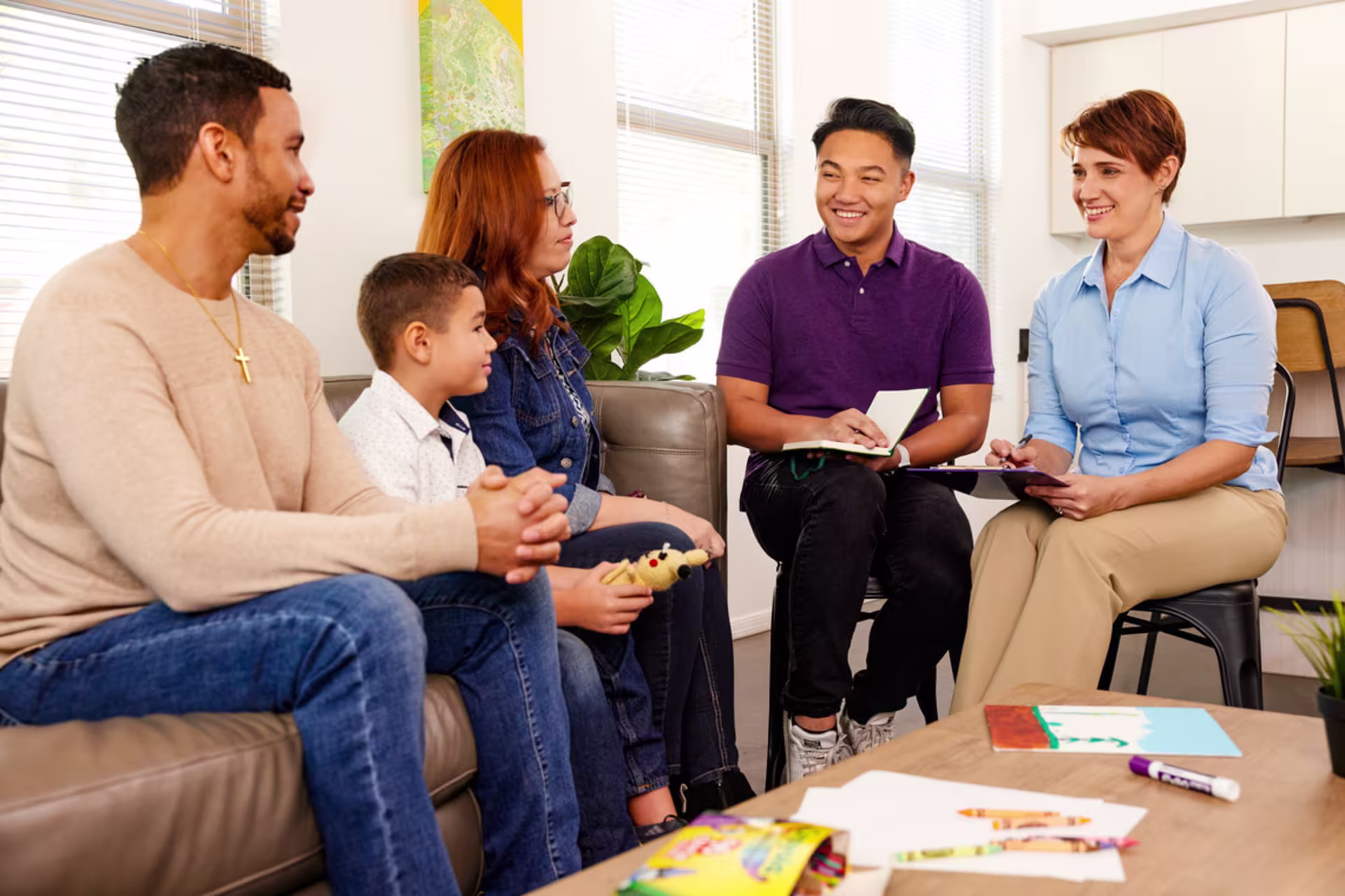 Two therapists lead a family counseling session with parents and a child in a supportive office setting.
