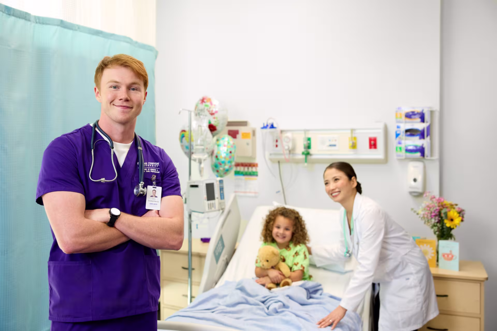 A nursing student and a registered nurse stand in a pediatric hospital room with a young patient.