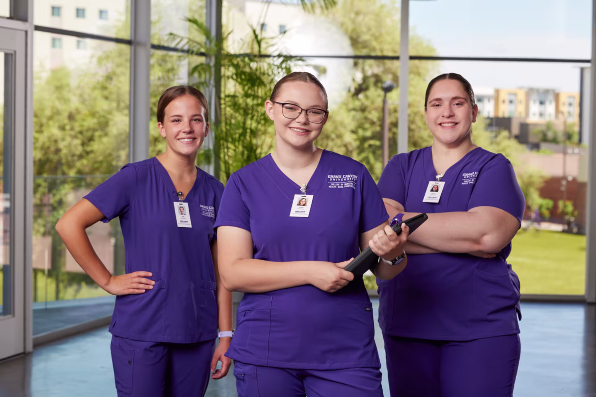 Female nursing students pose in front of a camera, wearing purple GCU-branded scrubs.