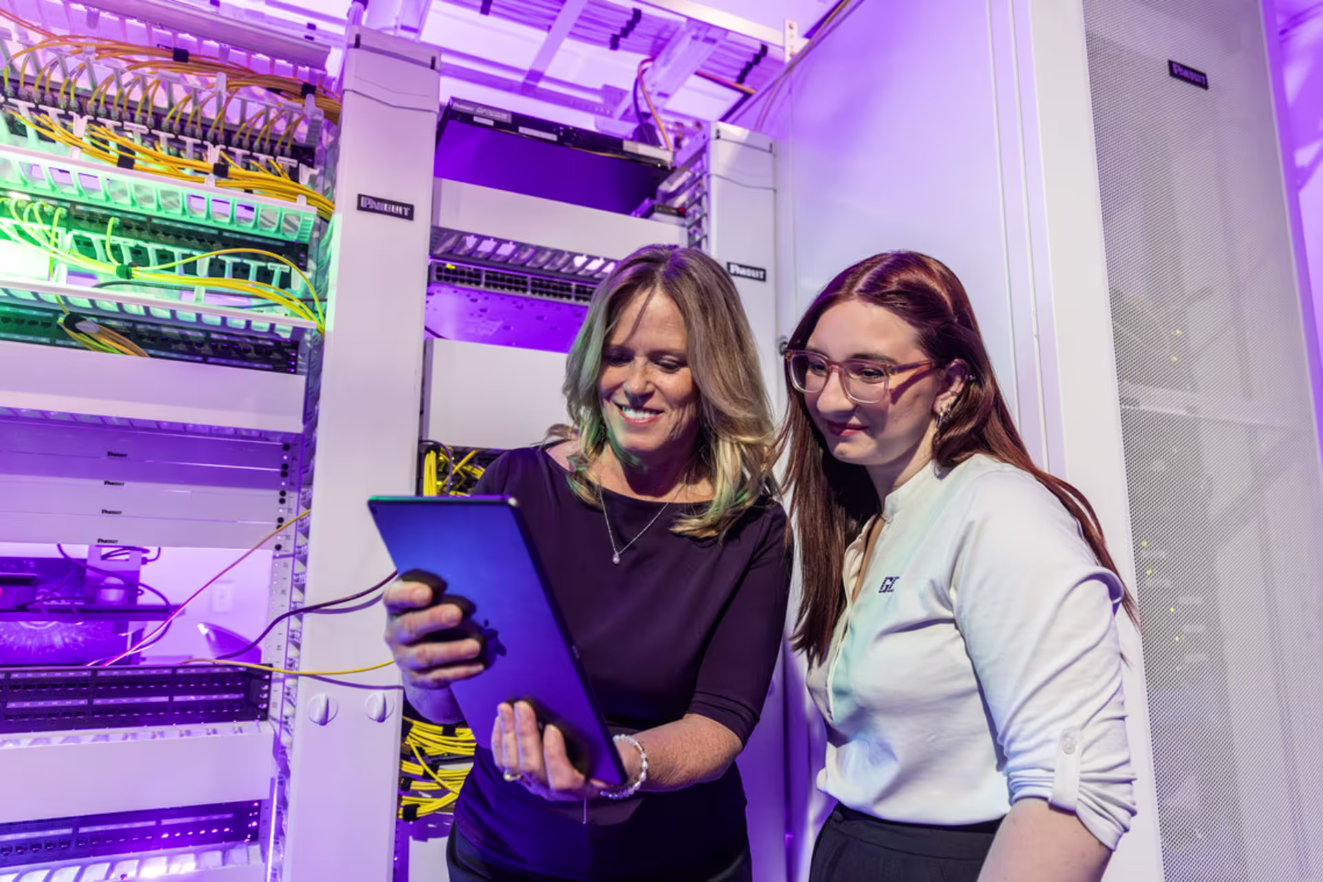 Cybersecurity professionals review network systems on a tablet in a server room.