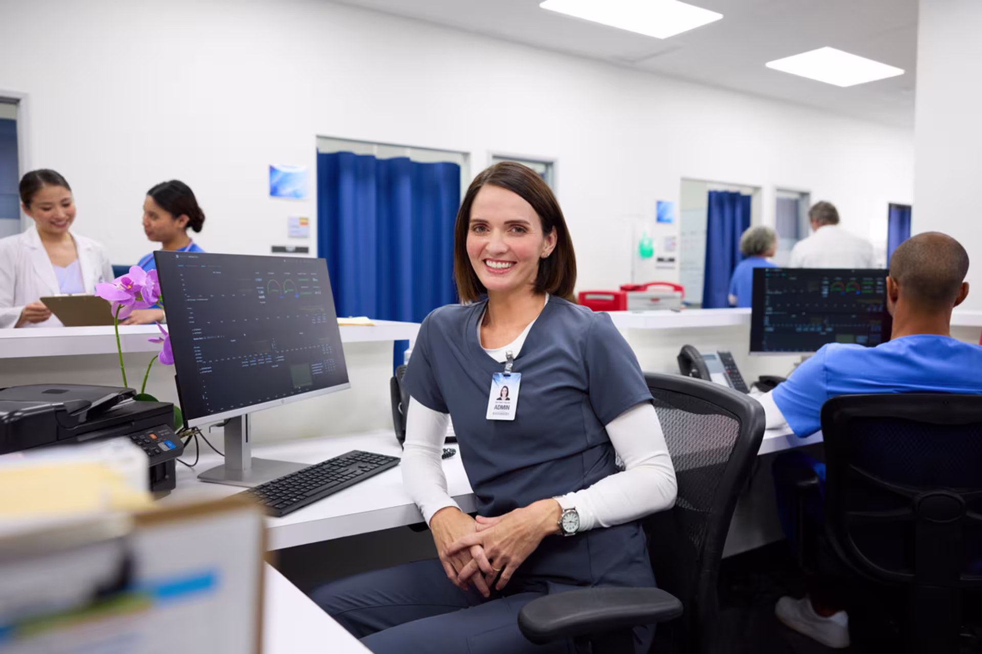 A nurse seated at a workstation monitors electronic health records.