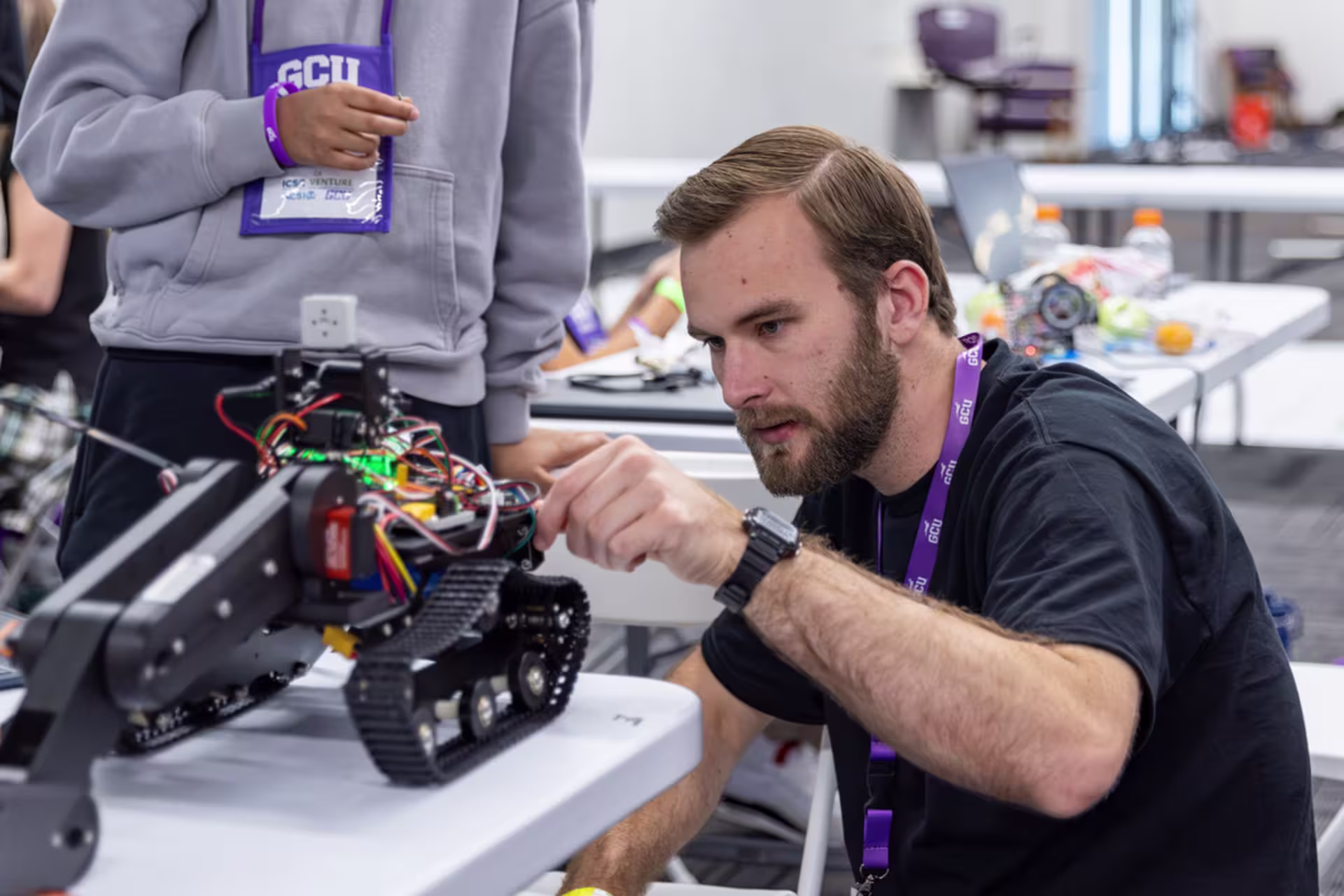 Male bearded GCU student adjusts settings in a robot-like device on a table with another person behind him observing.