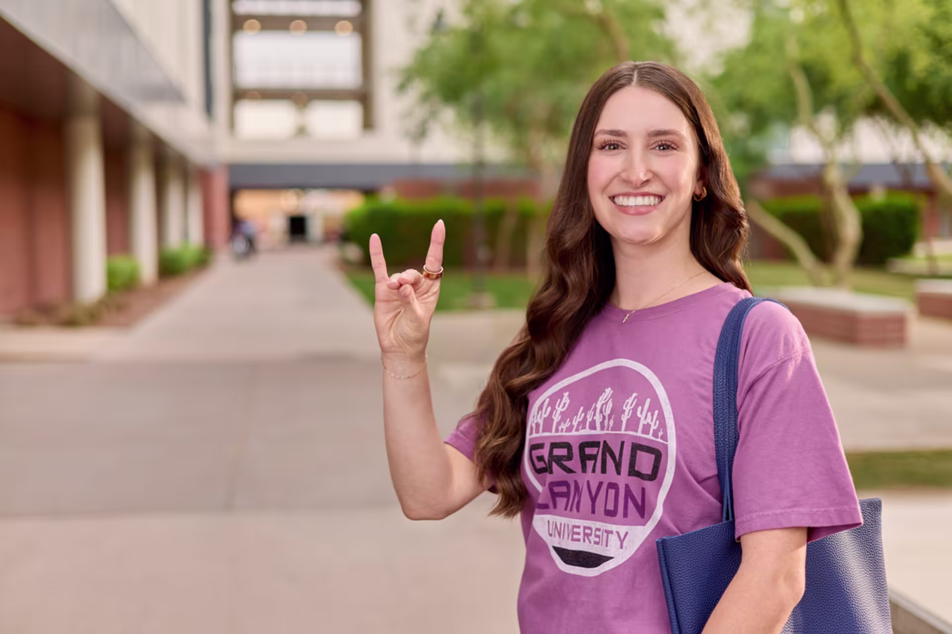 A female business student stands outside holding the Lopes Up hand sign while smiling at the camera.