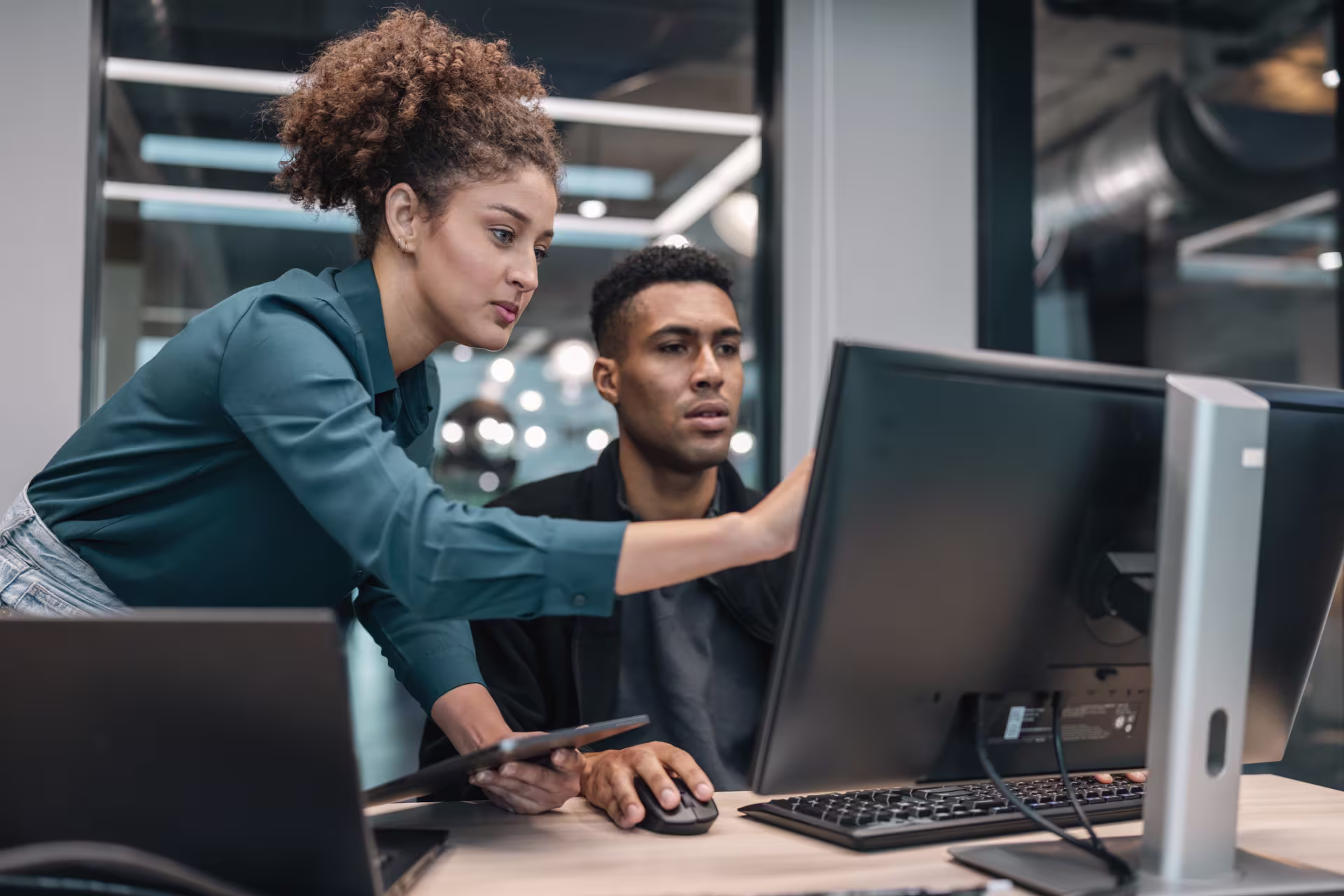Two professionals review location-based data on a computer and tablet in a modern office, illustrating geofencing technology and analytics.