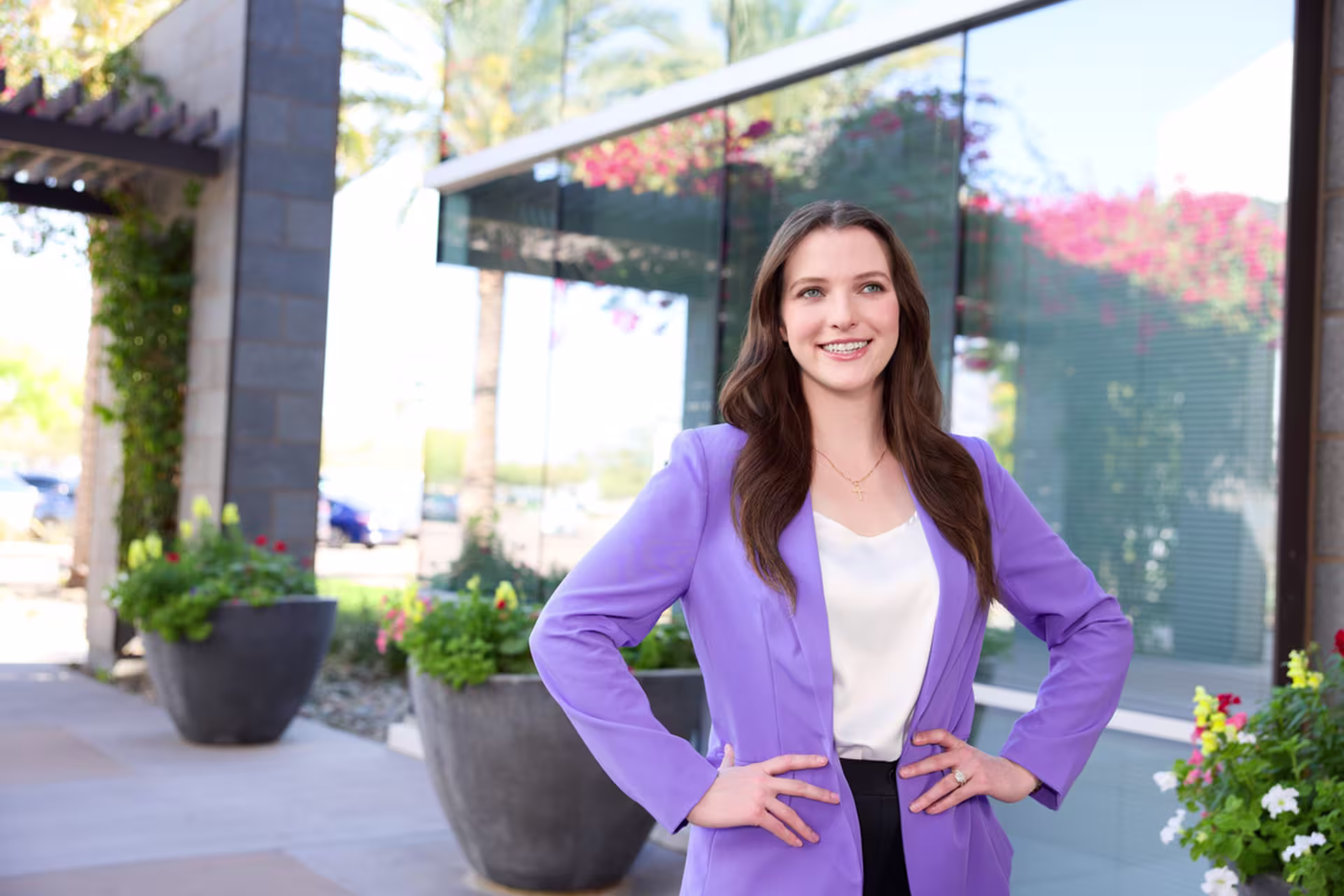 Female doctoral student in a purple blazer standing outside with her hands on her hips and smiling.