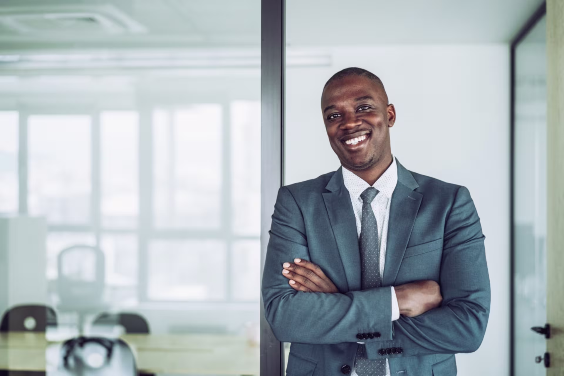 A smiling male accountant wearing a suit stands with his arms crossed in a modern office.