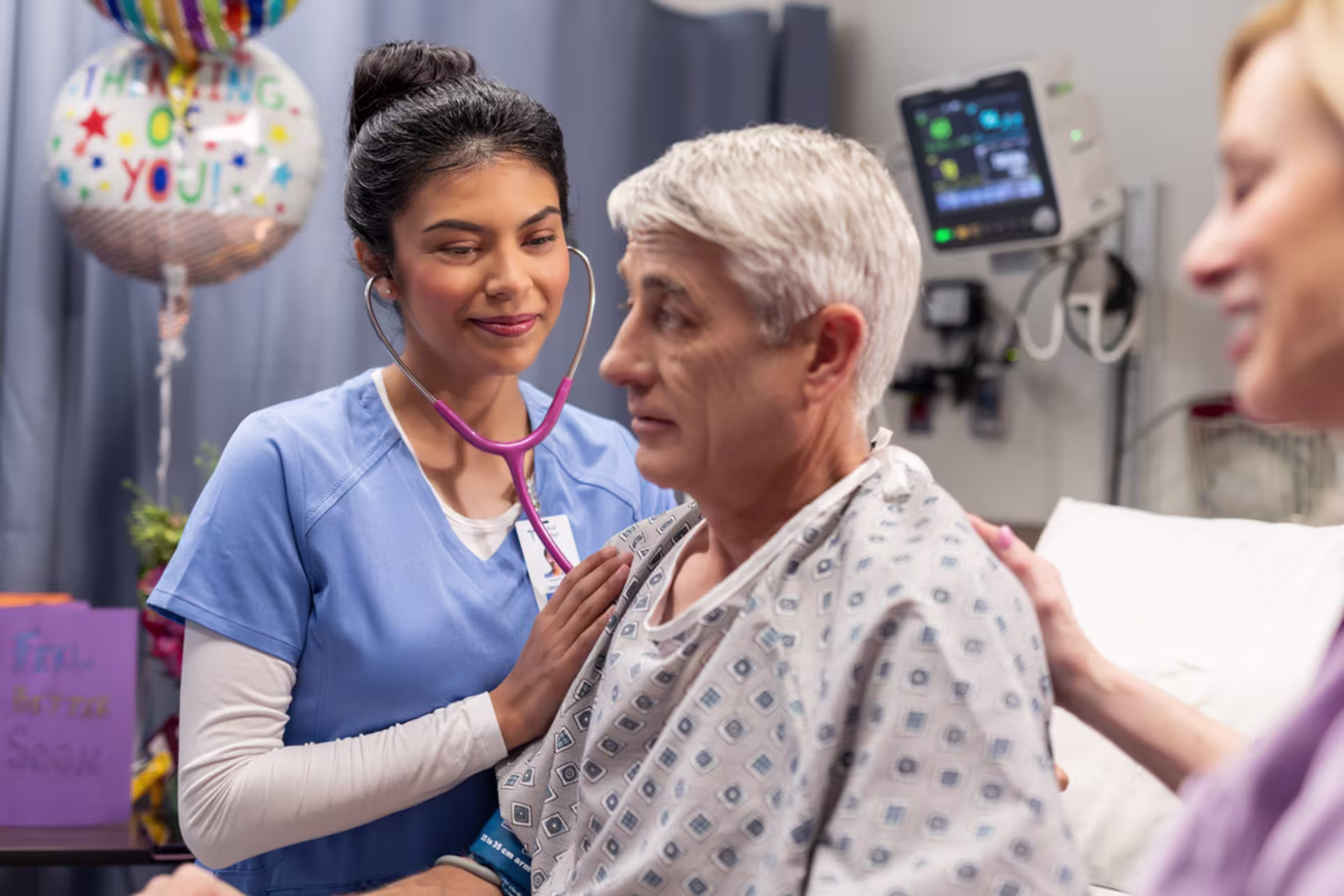 Nurse using a stethoscope to examine an older patient sitting in a hospital bed.