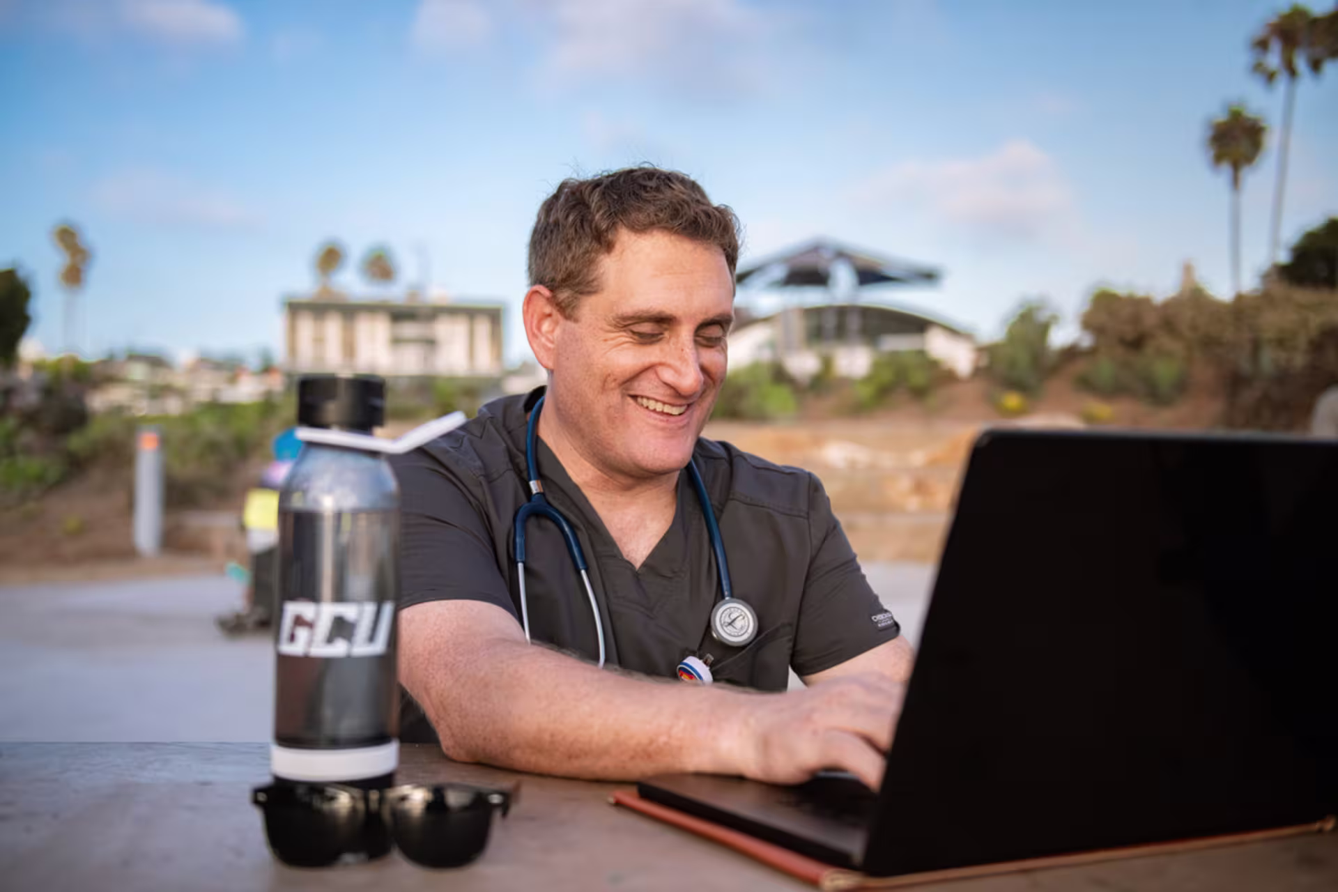 Male nurse using a laptop outdoors with a stethoscope.