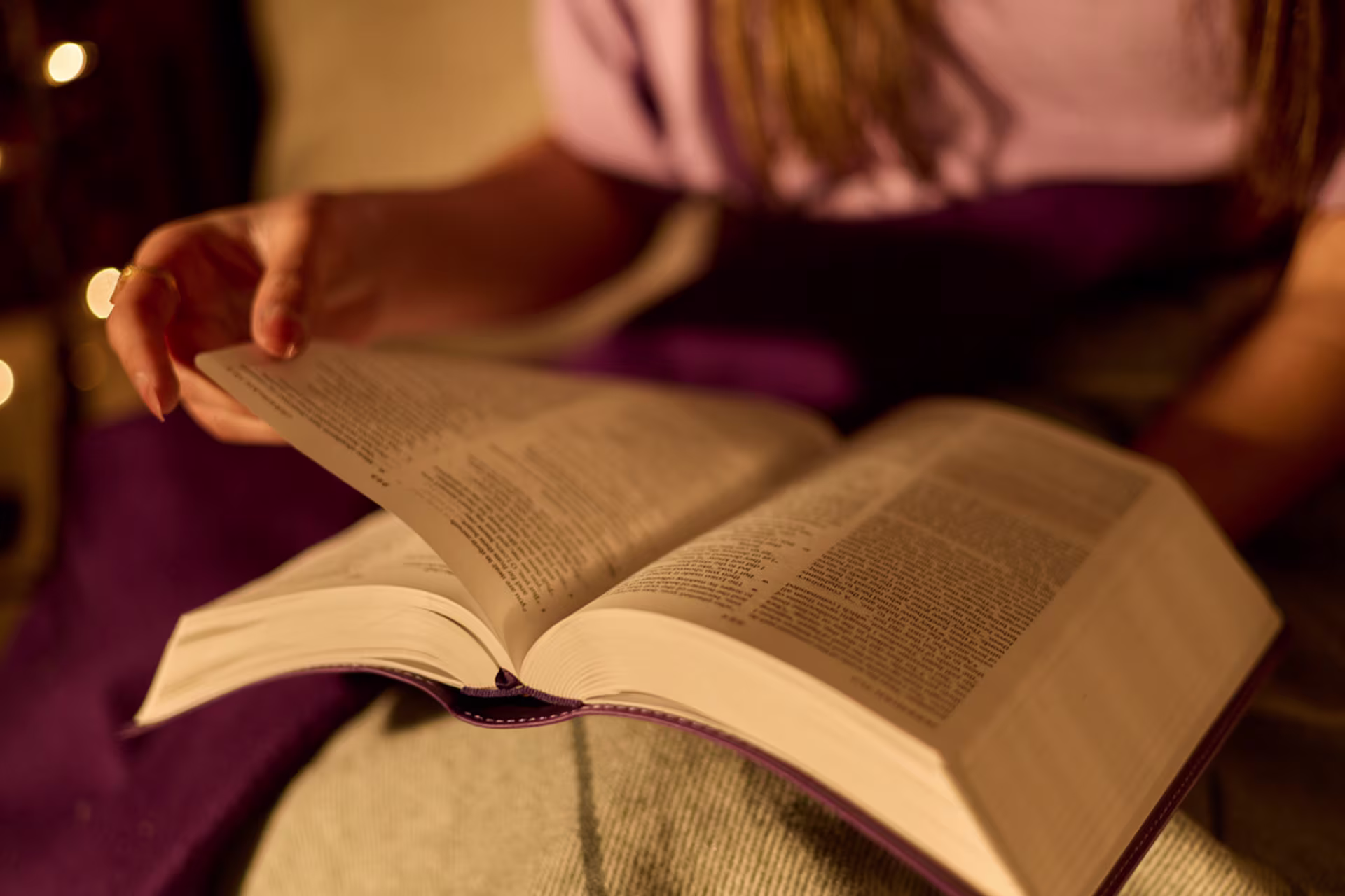 A person turns pages in a Bible while reading at home.