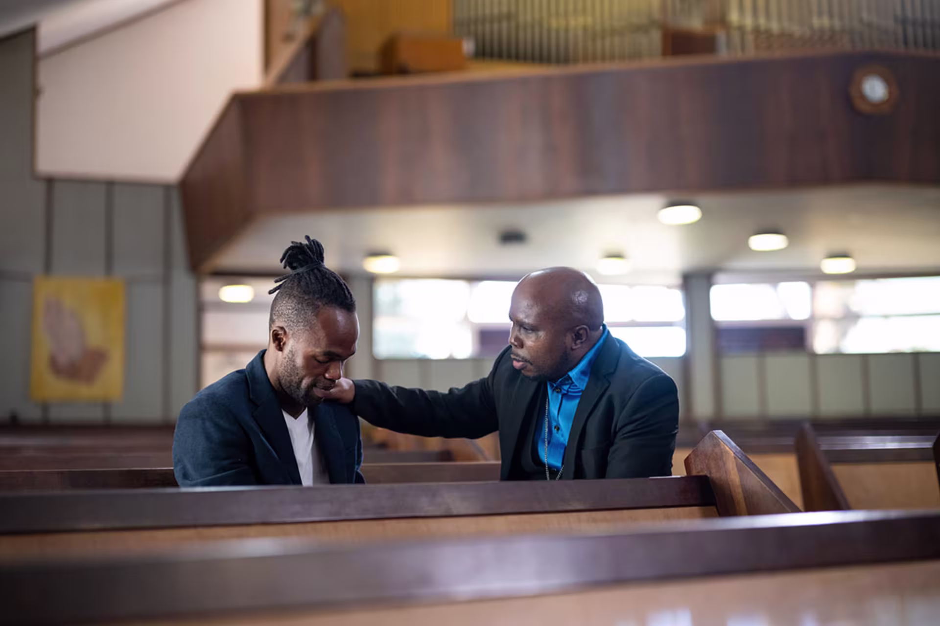 Pastor counseling and offering support to a church member seated in a pew.