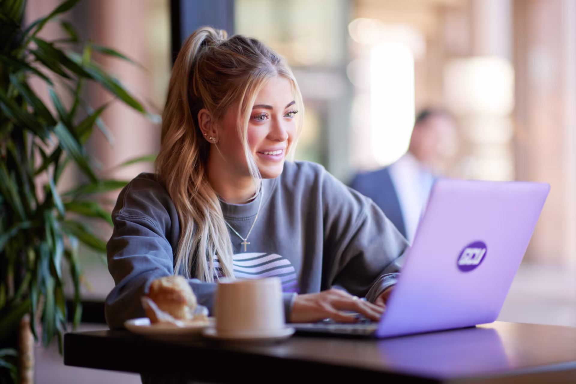 A female student studies online on a laptop at a coffee shop.