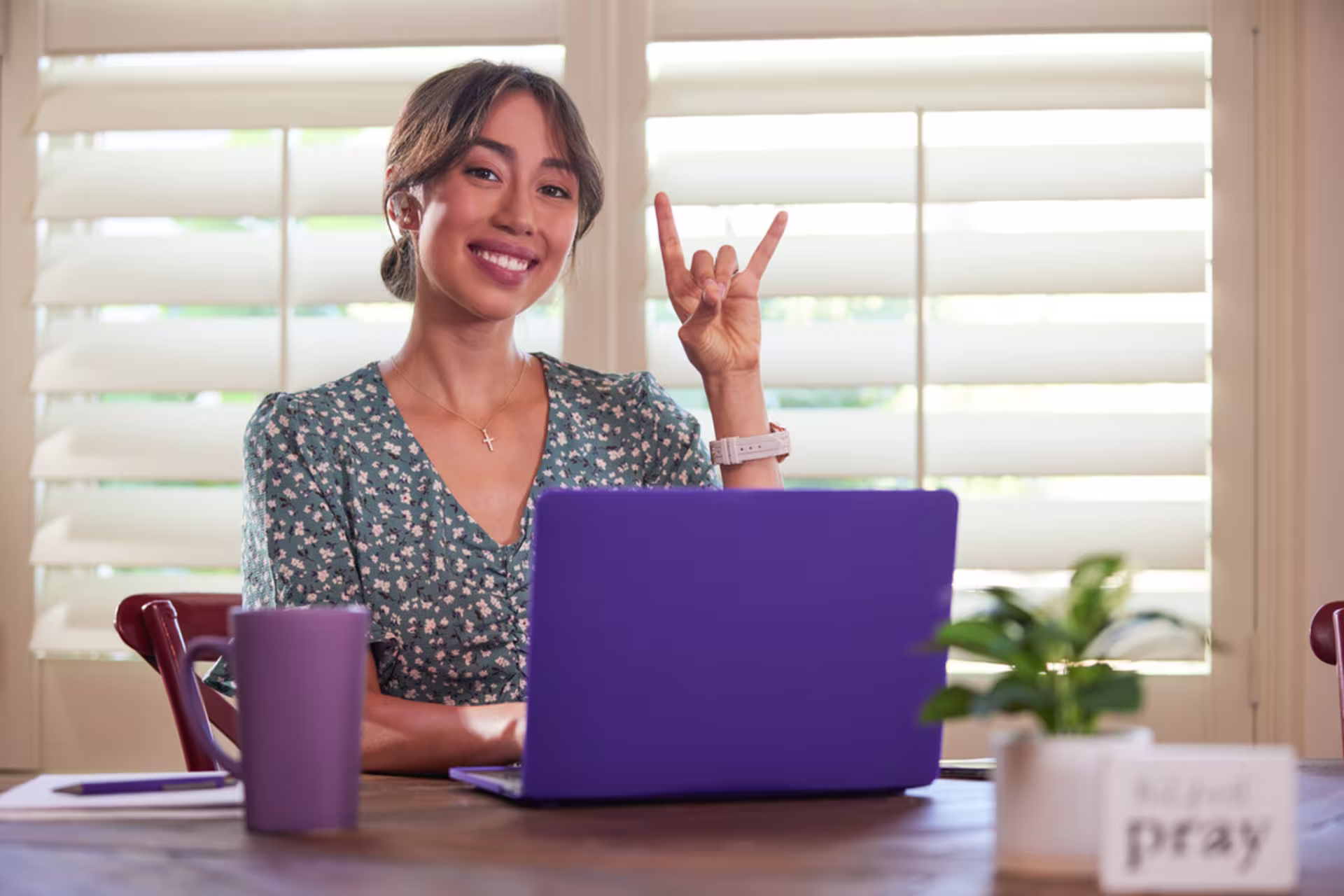 A student smiles during a virtual class on a laptop from home while holding the Lopes Up hand sign.