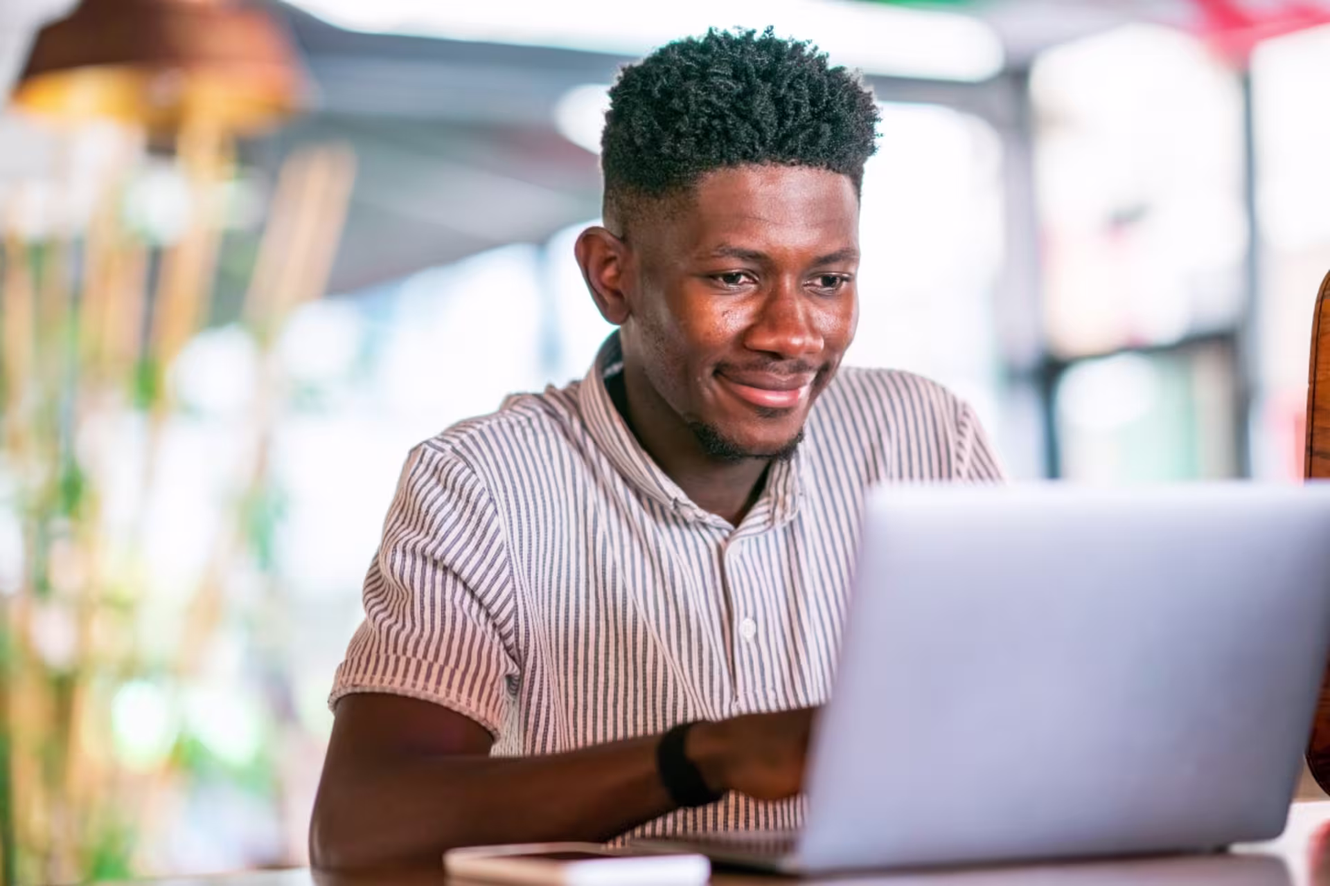 A male social media student smiles while studying online with a laptop.