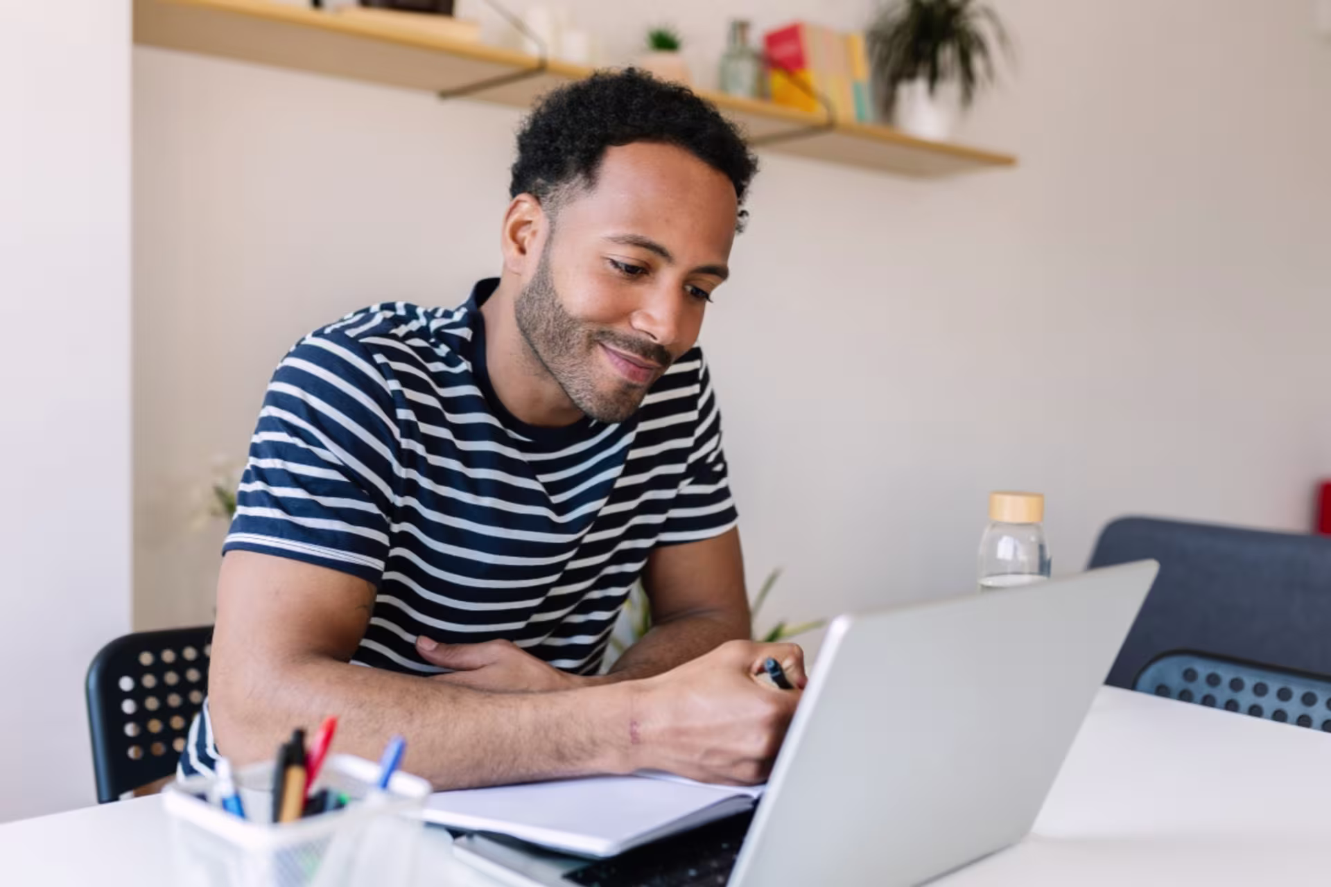 A male social media student takes notes while learning on a laptop.
