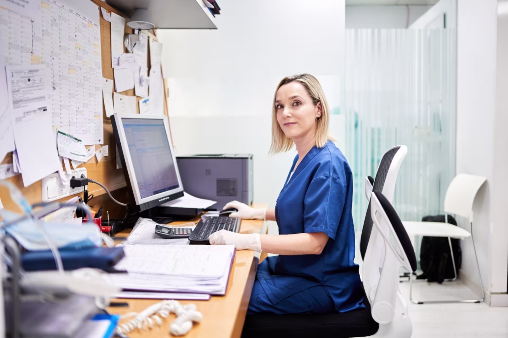 Female health administration professional working at a computer in a healthcare facility.