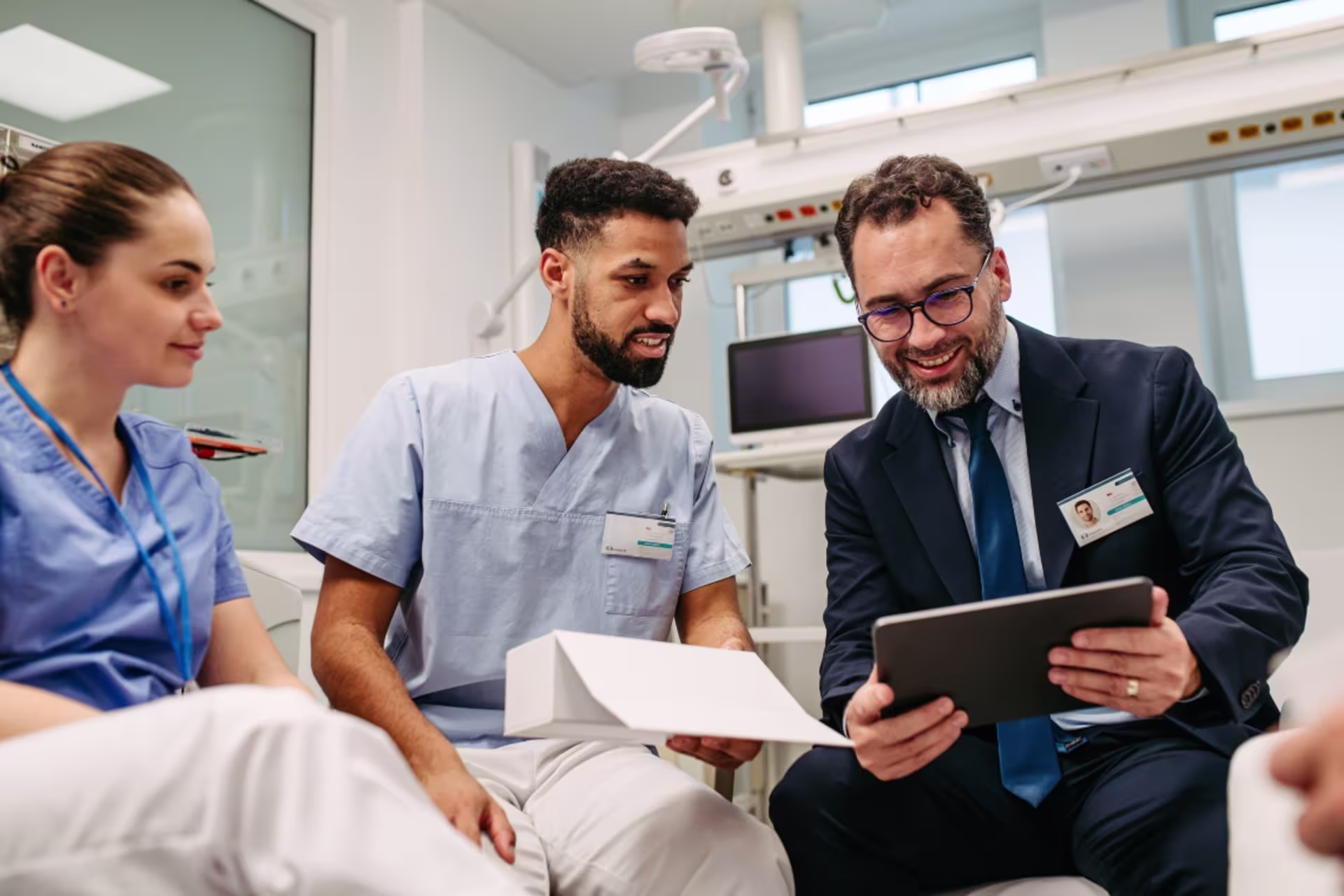 Male health administration professional reviewing information on a tablet with healthcare staff.