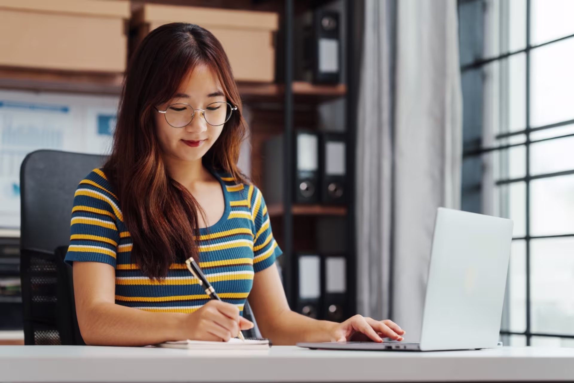 A master’s communications student takes notes while working on a laptop.