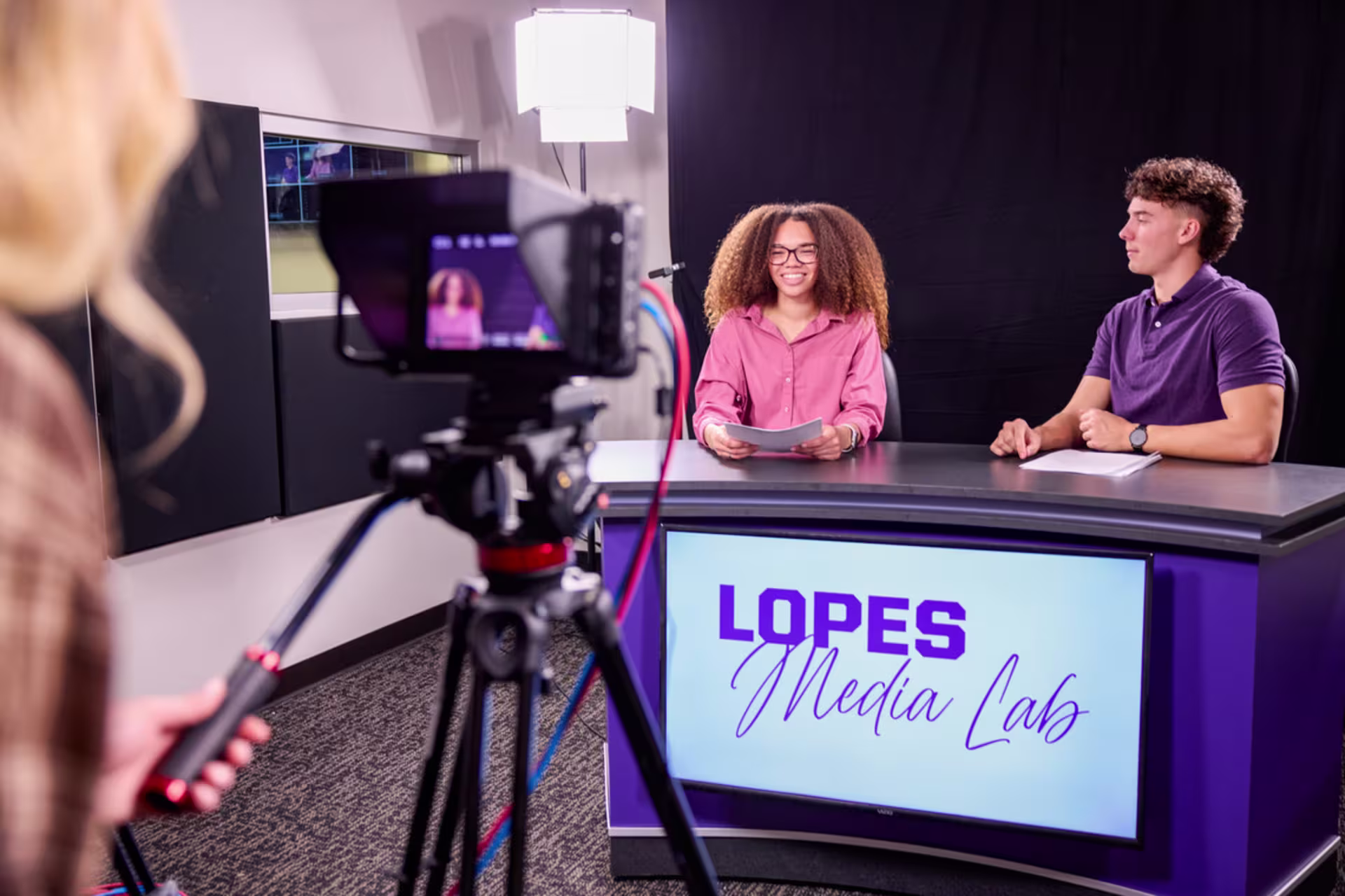 Sports broadcasting students presenting a news segment in a media studio.