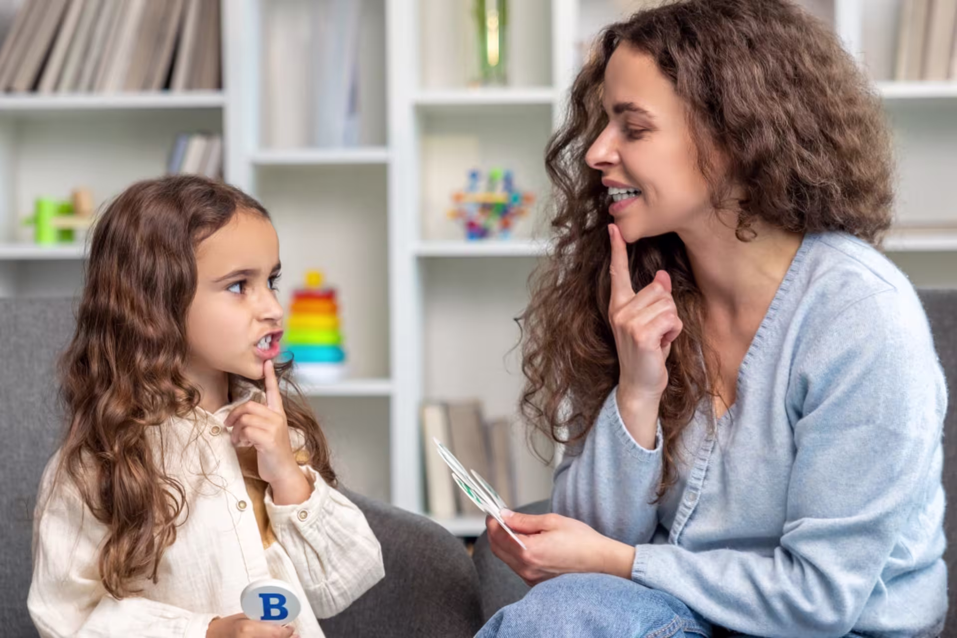 Female speech language pathology professional guiding a child through a speech exercise.
