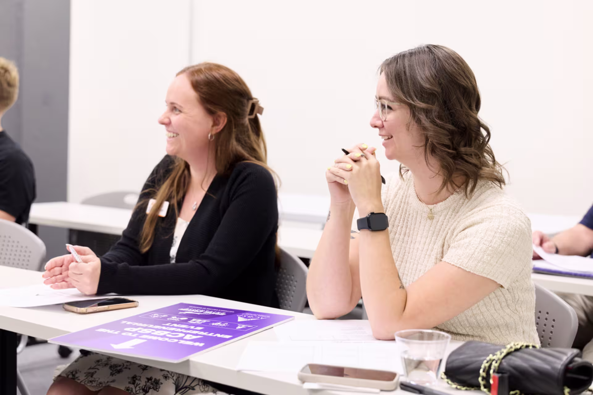 Female business administration students present their project while sitting at a table in a class setting.