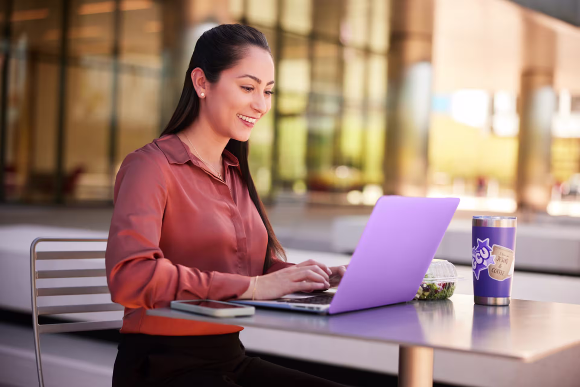 Female counseling student smiling and working on a laptop between classes.