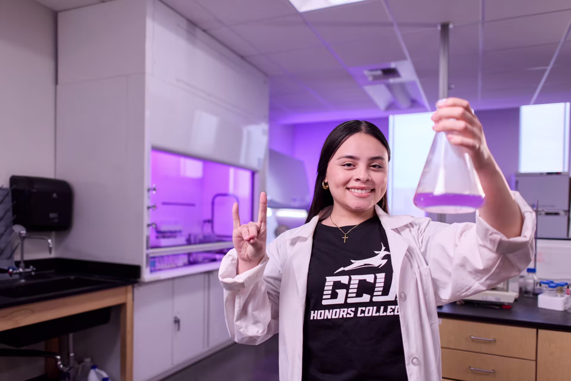 Female biology student holding a flask and making the Lopes Up hand gesture.