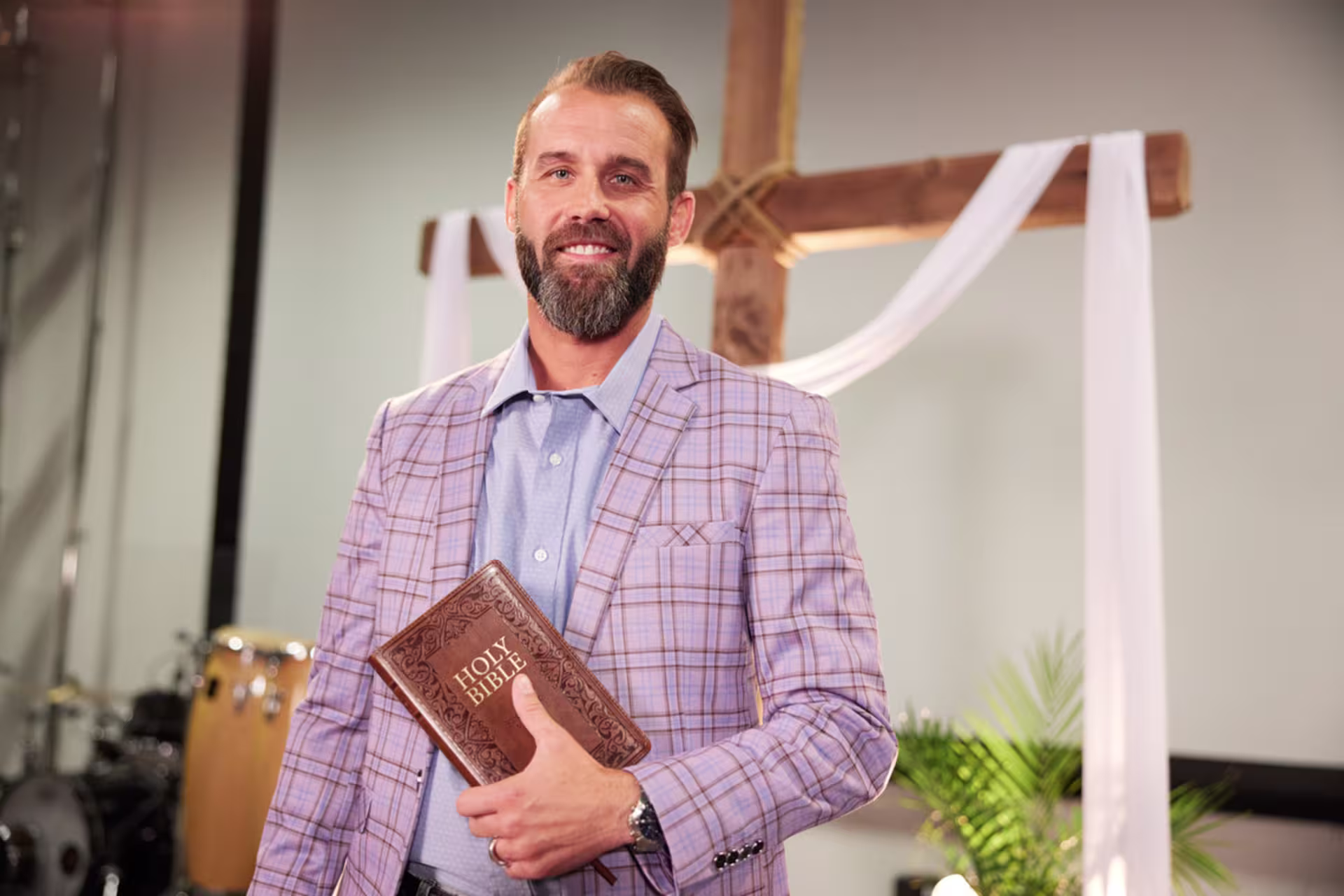 Church leader holding a Bible while standing in front of a cross during a church service.