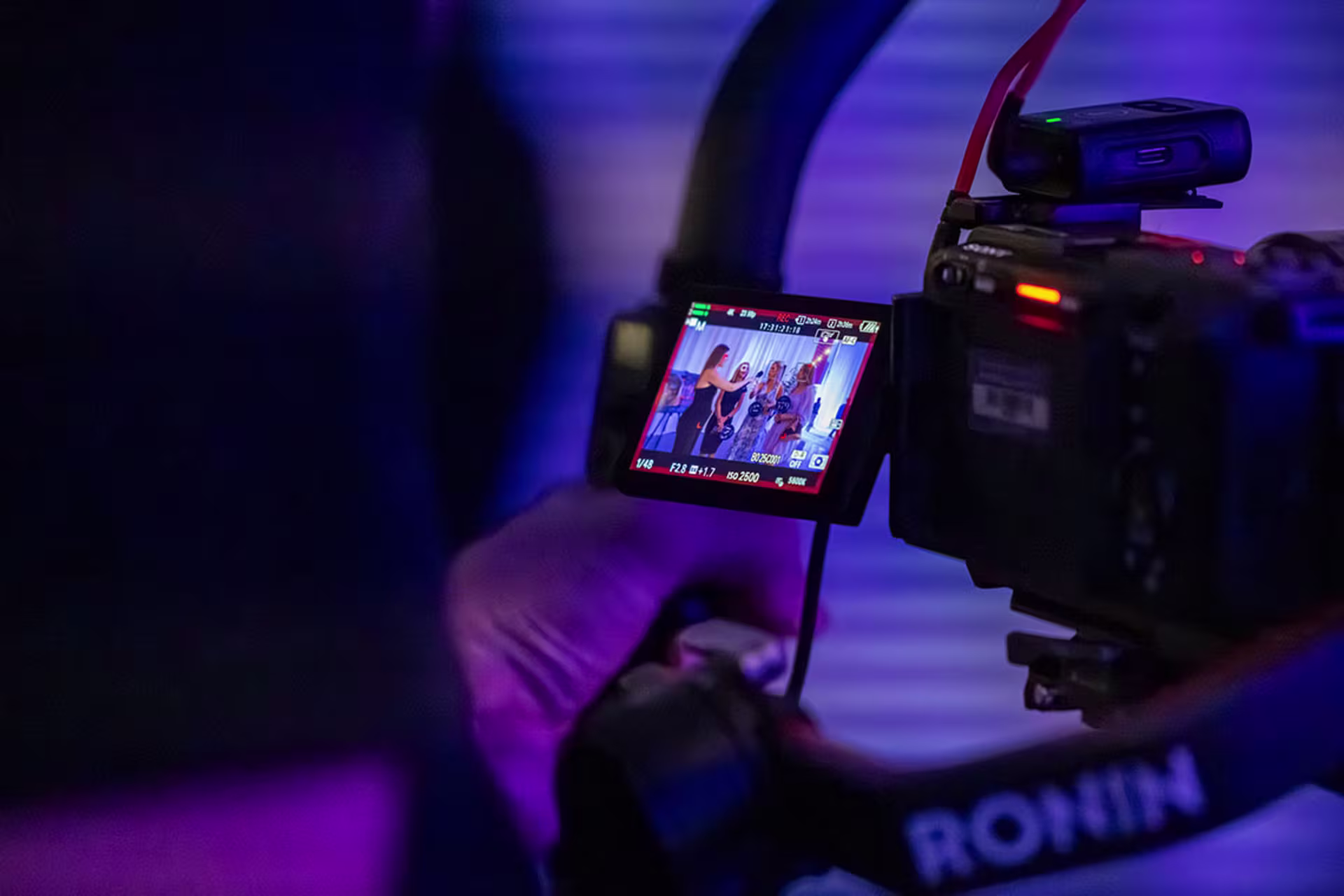 Professional video camera recording speakers at a live event with the camera monitor showing the stage.